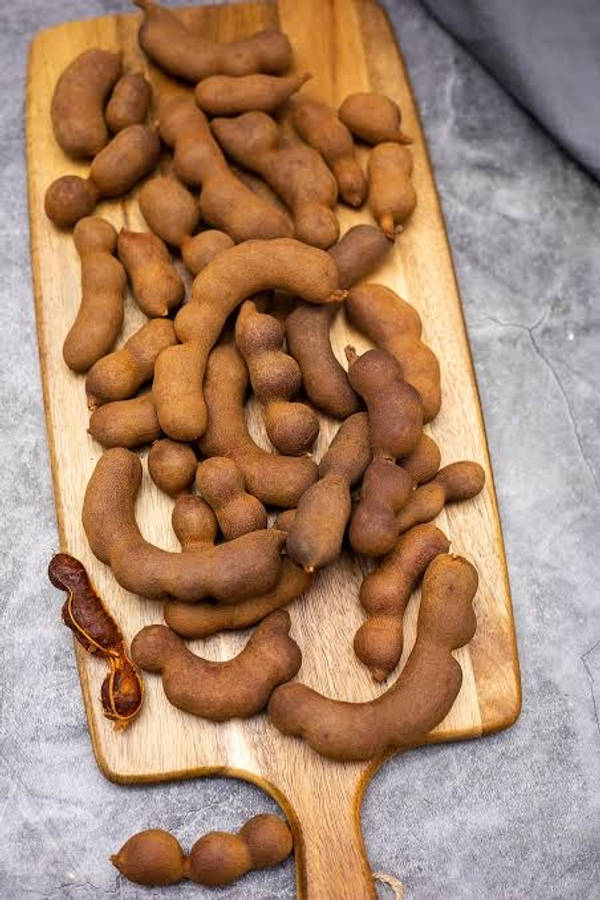 beans 桌布 壁紙 — 一個木製砧板上堆滿棕色羅望子莢，置於灰色石面上。