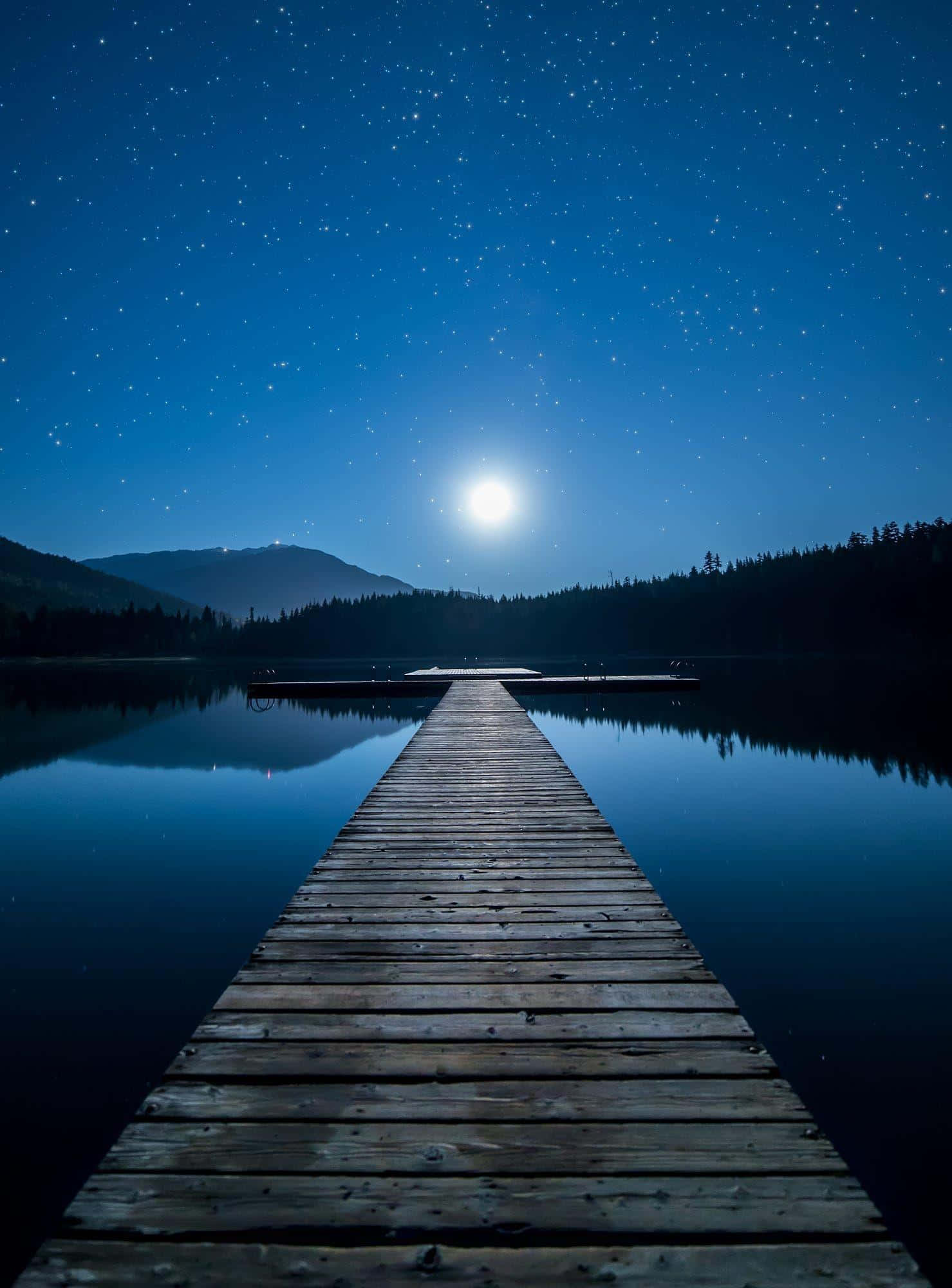Moonlight 桌布 壁紙 — 一個木製碼頭在明亮的滿月下延伸至星空夜湖，遠處有山巒。