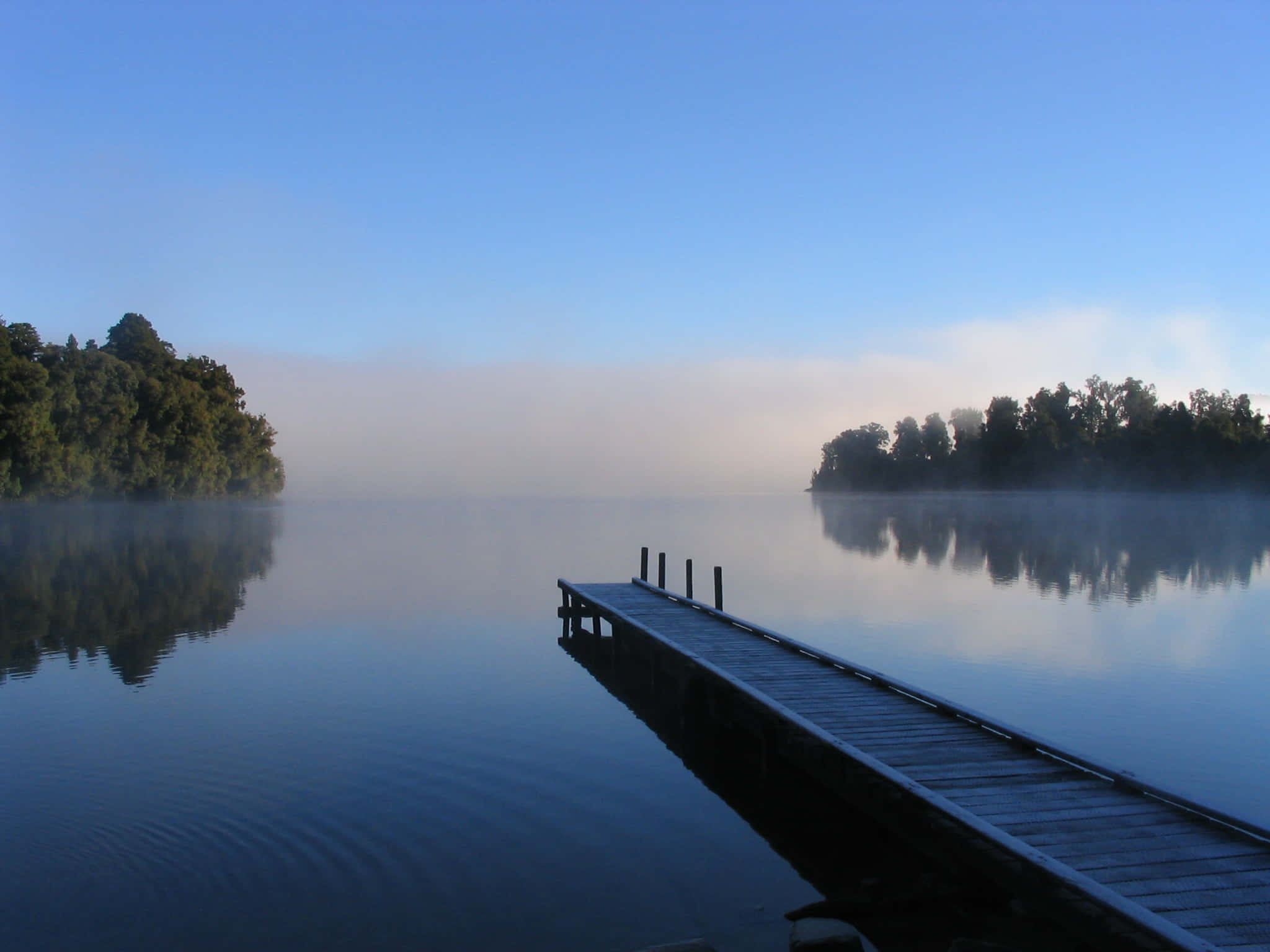 Lake 桌布 壁紙 — 一個木製碼頭在黎明時分延伸至霧氣瀰漫的湖泊，平靜的水面倒映著樹木和天空。