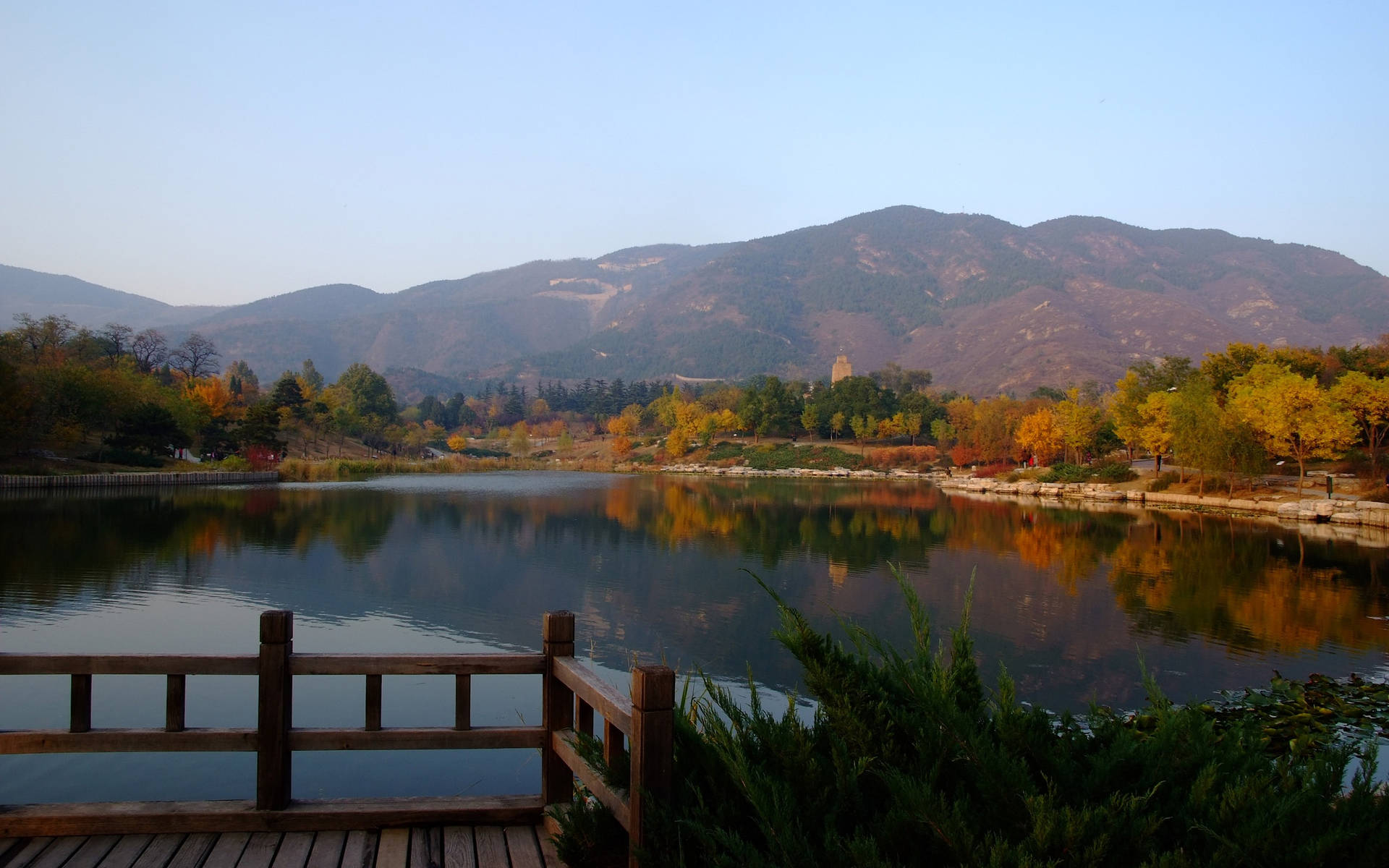 湖邊的木製碼頭，背景有秋樹和山脈 — 4K秋日壁紙 壁紙
