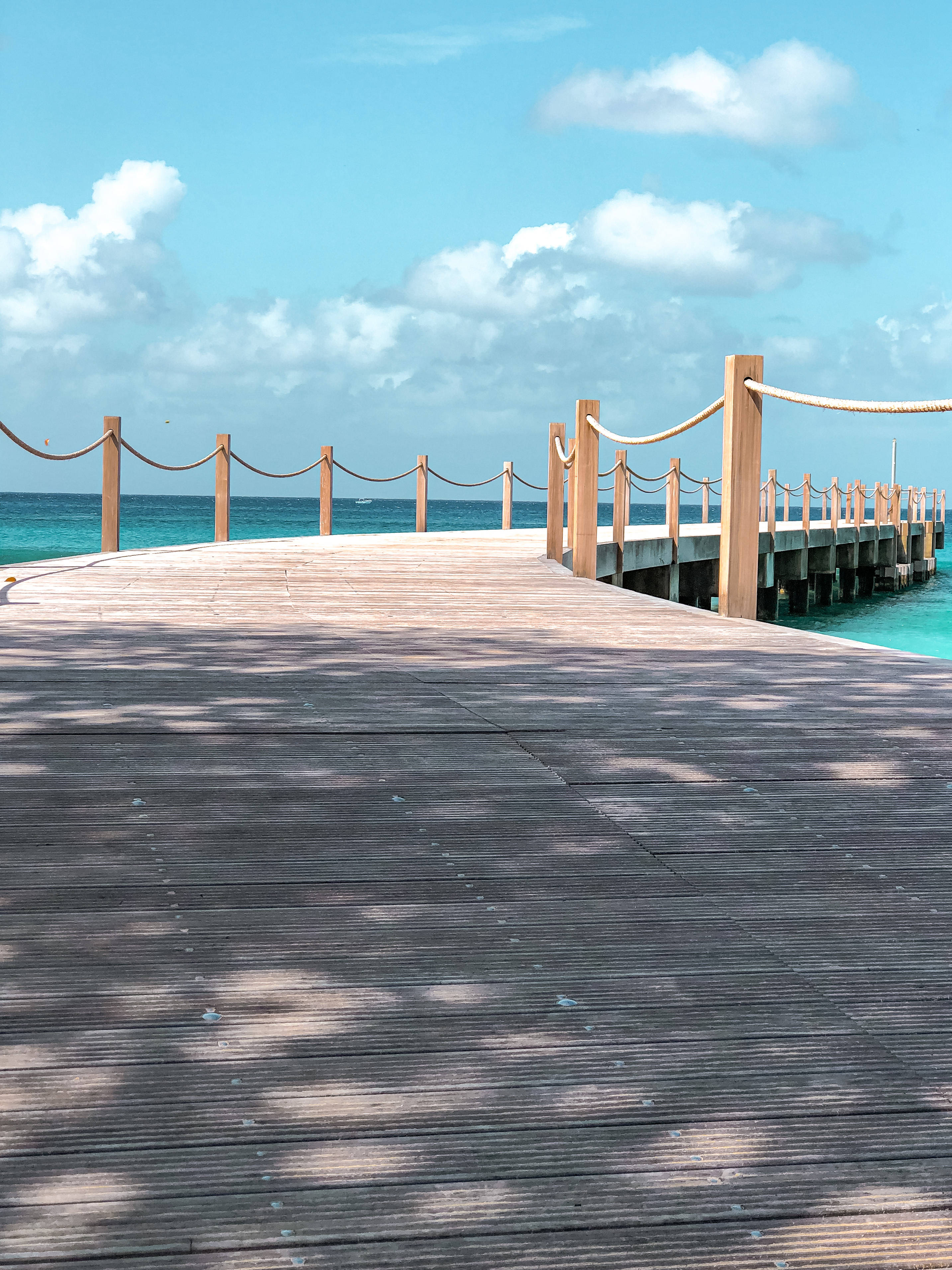 Barbados 桌布 壁紙 — 一個木製碼頭延伸至藍綠色的海洋，上方是明亮的藍天和蓬鬆的白雲。