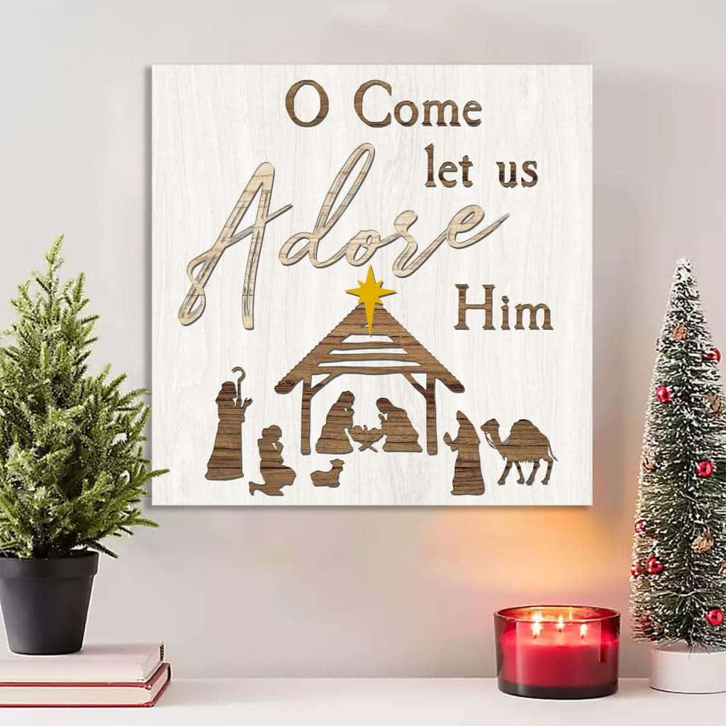 Religious Christmas 桌布 壁紙 — 一個木製耶穌誕生場景，上面掛著「O Come let us Adore Him」的文字，下方有一根點燃的蠟燭，兩側各有一棵小聖誕樹。