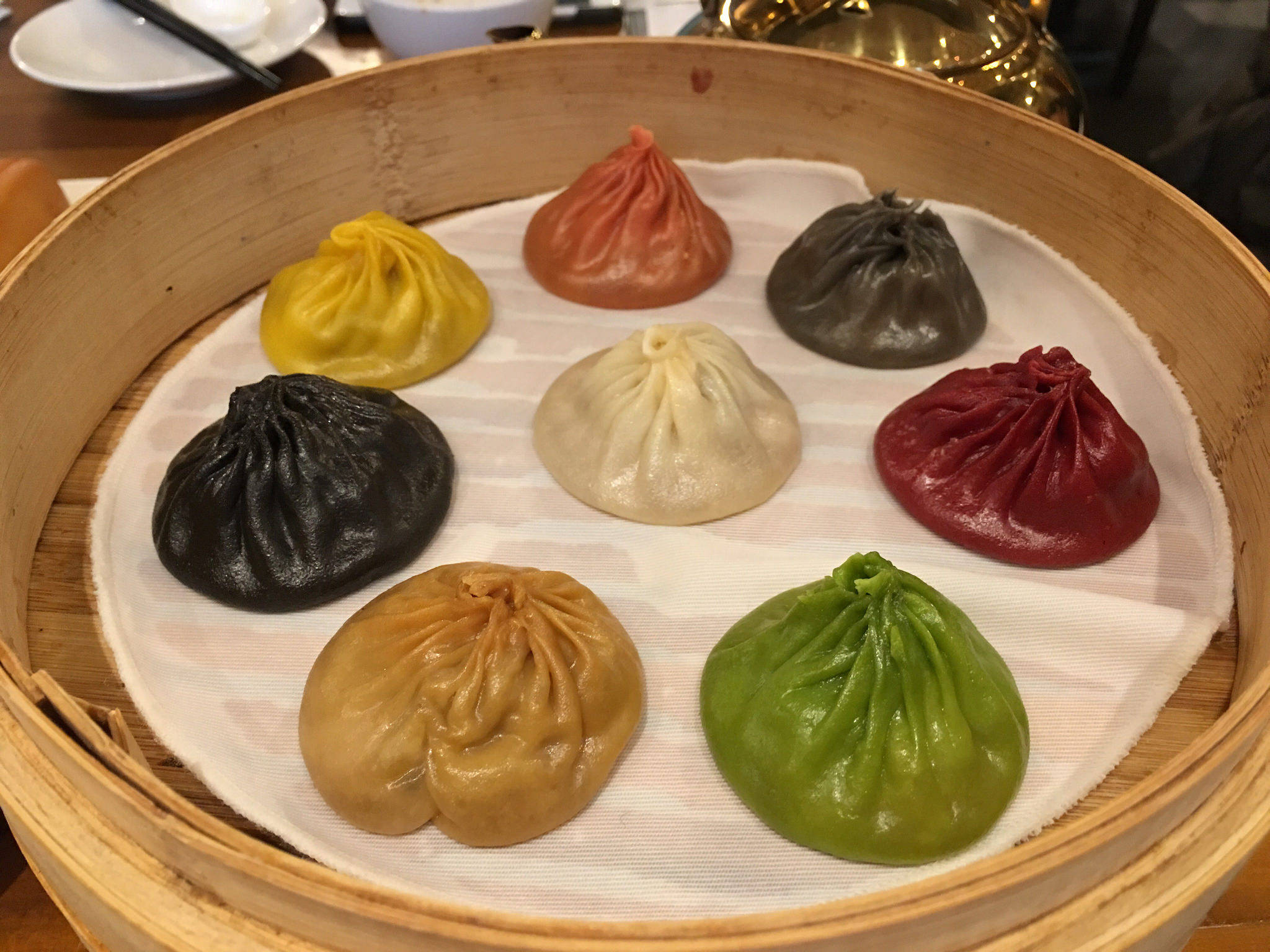 steam 桌布 壁紙 — 一個木製蒸籠裝有七個色彩繽紛的餃子，色調鮮豔，包括黃色、紅色、黑色、綠色、米色和棕色。