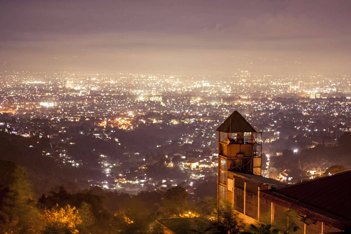 bandung 桌布 壁紙 — 一個木製觀景塔俯瞰著廣闊的城市景觀，在暮色紫羅蘭色的天空下閃爍著燈光。