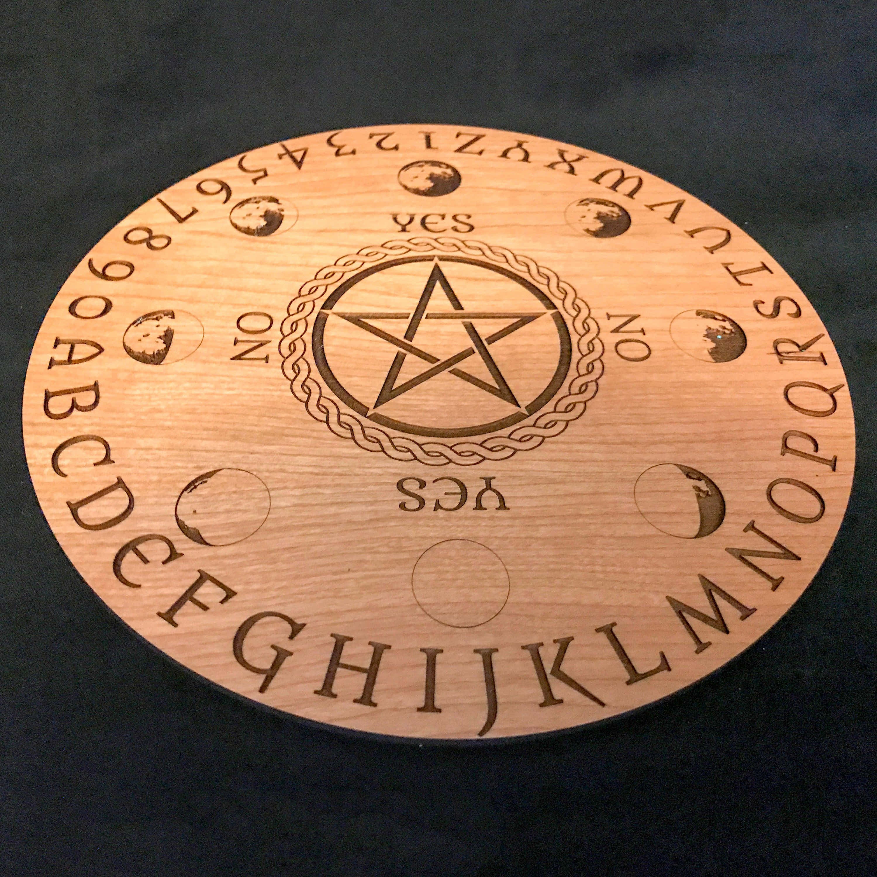 Ouija Boards 桌布 壁紙 — 一個木製通靈板，上面刻有字母、數字、五角星和月亮相位，背景為深色。