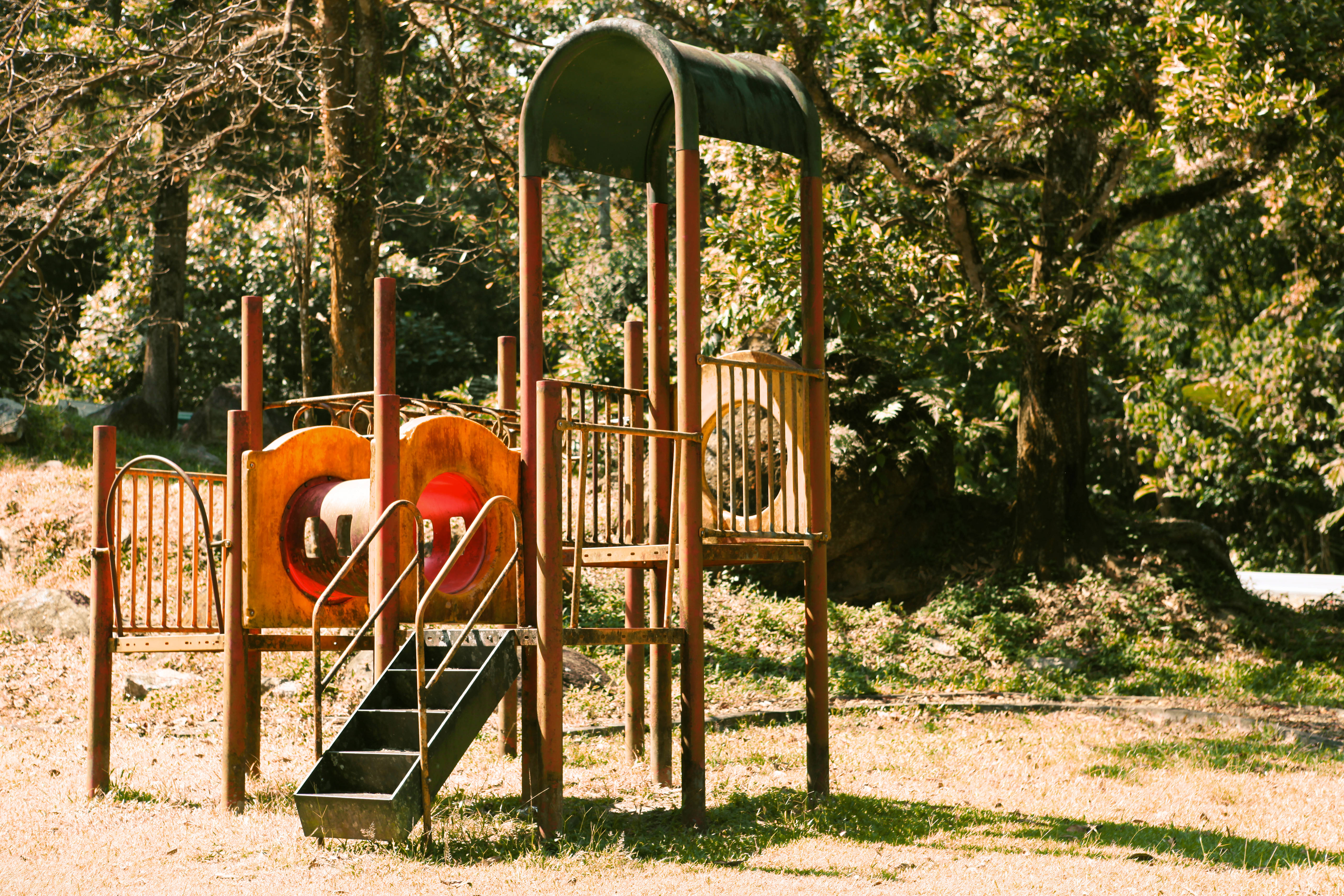 Playground 桌布 壁紙 — 一個木製遊樂場結構，帶有紅色溜滑梯和綠色遮陽篷，矗立在陽光明媚的森林空地上。