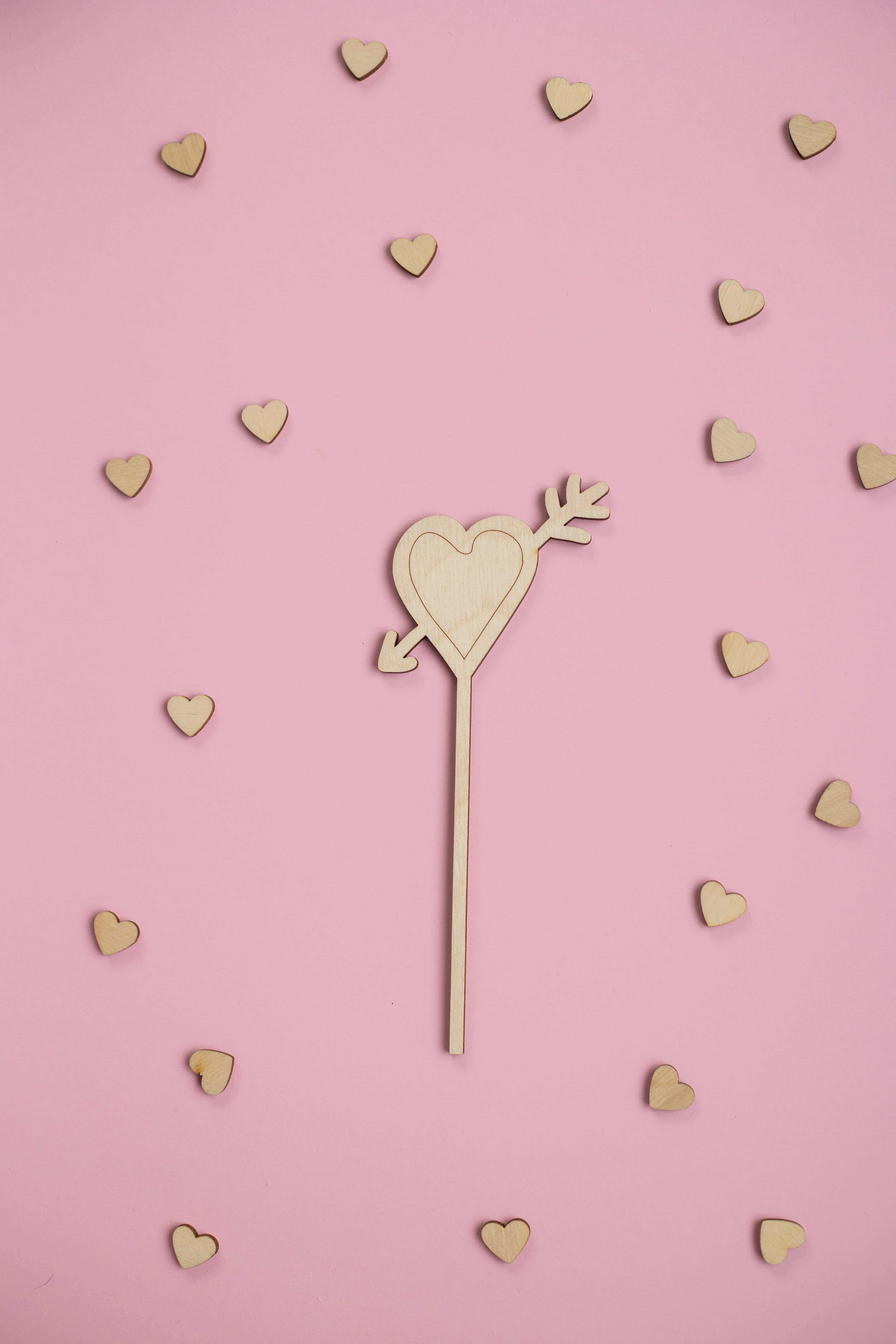 Glitter Pink Hearts 桌布 壁紙 — 一個木製邱比特箭，箭頭為心形，立於柔軟粉紅色背景上散落的小木心之間。