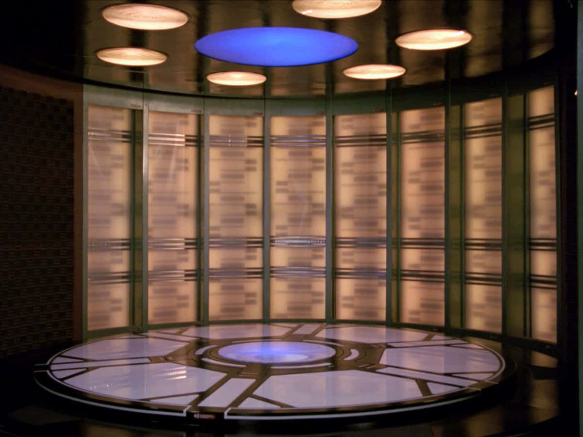 Star Trek Enterprise Bridge 桌布 壁紙 — 一個未來風格的圓形房間，帶有發光的藍色天花板和地板面板，周圍是帶有溫暖背光的玻璃牆。