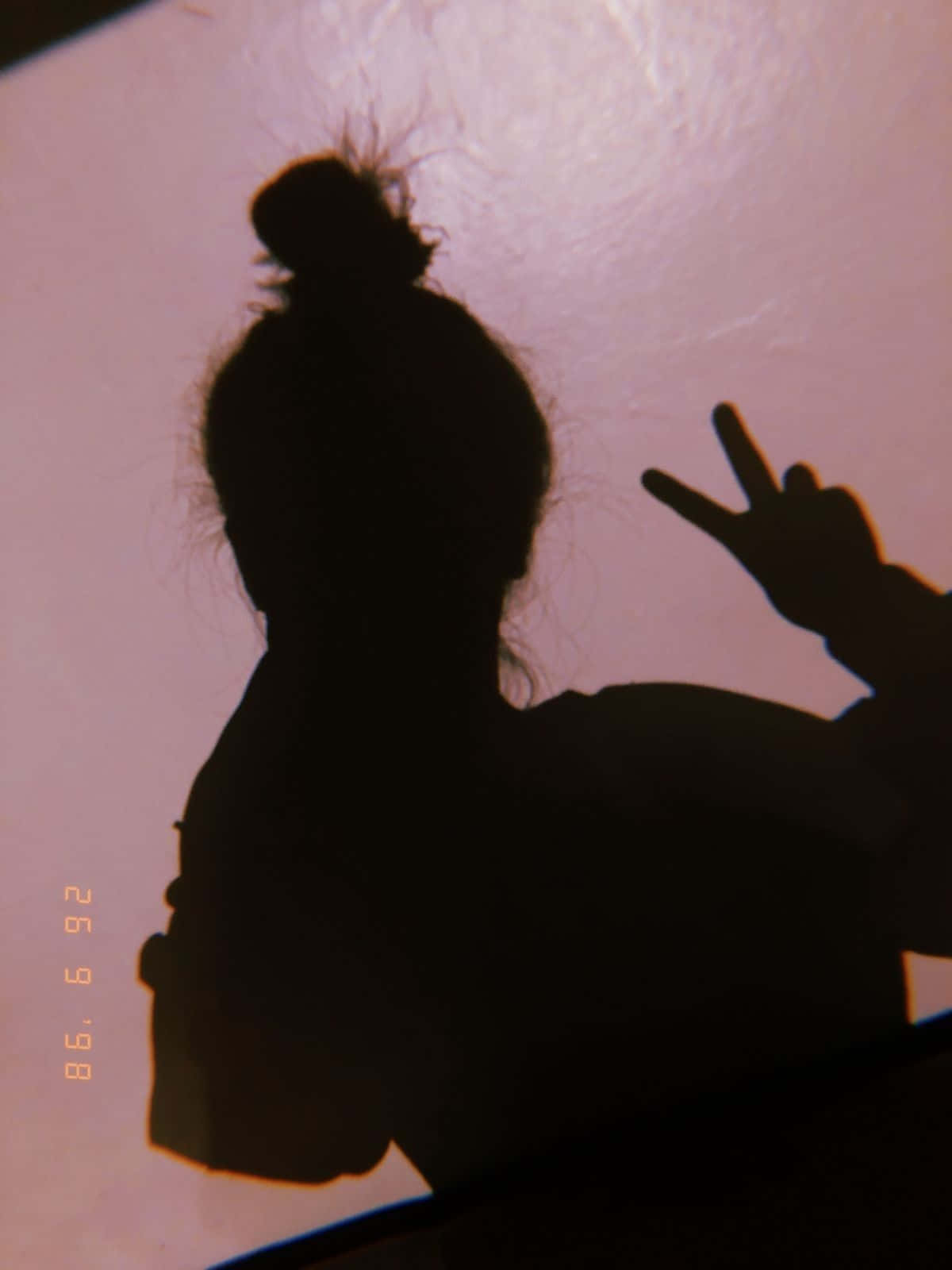 reflection 桌布 壁紙 — 一個束著髮髻的人影，在柔和的粉紅色紋理牆前做出和平手勢。
