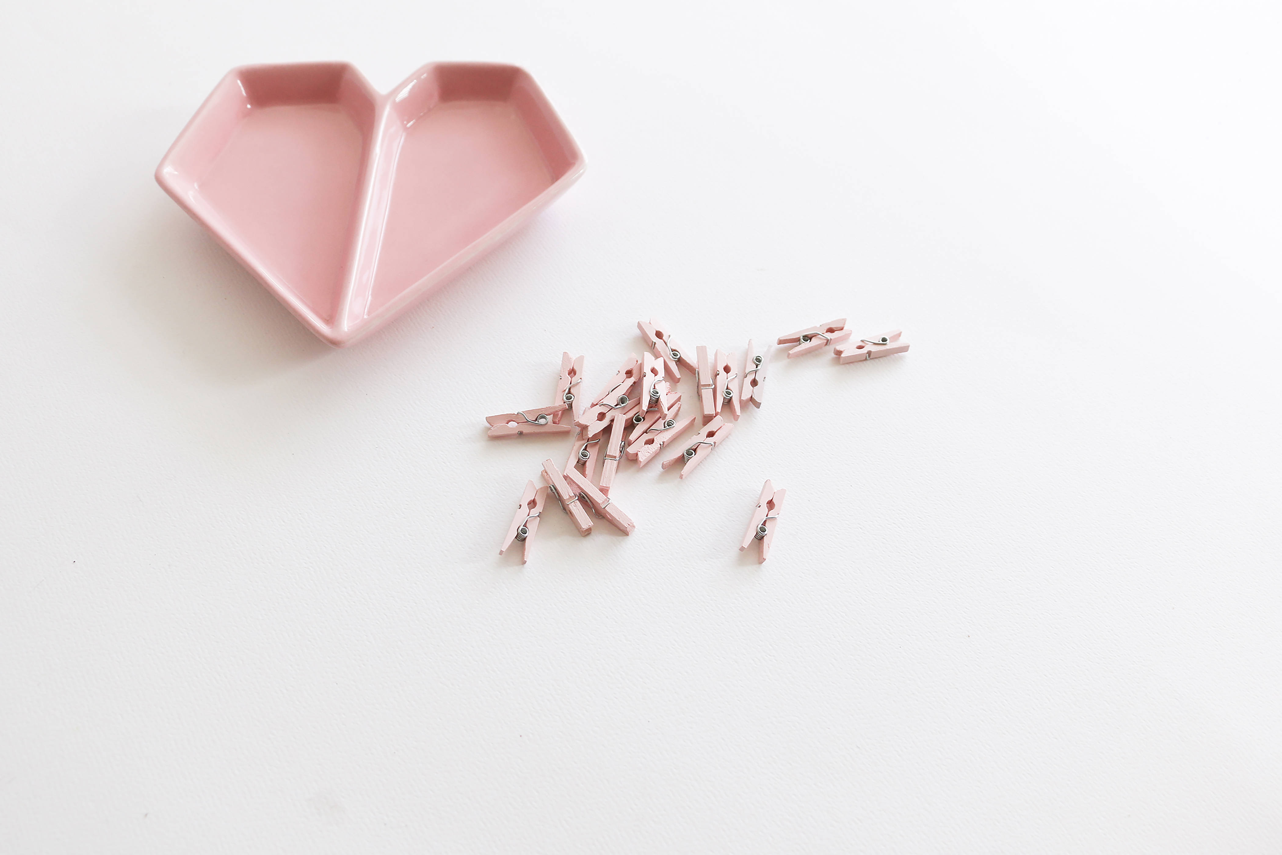 girly pink aesthetic 桌布 壁紙 — 一個柔軟的粉紅色心形盤子和散落的粉紅色衣夾放在潔白的表面上。