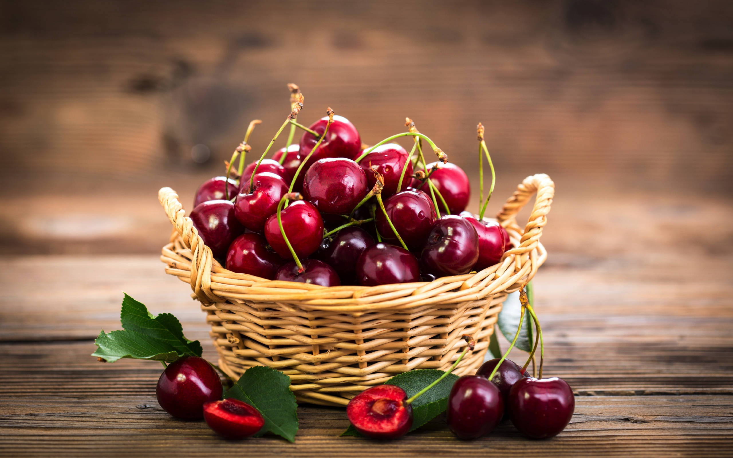 Fruit 桌布 壁紙 — 一個柳條籃子裝滿了光澤的紅色櫻桃，放在一張質樸的木桌上，旁邊散落著樹葉和半個櫻桃。