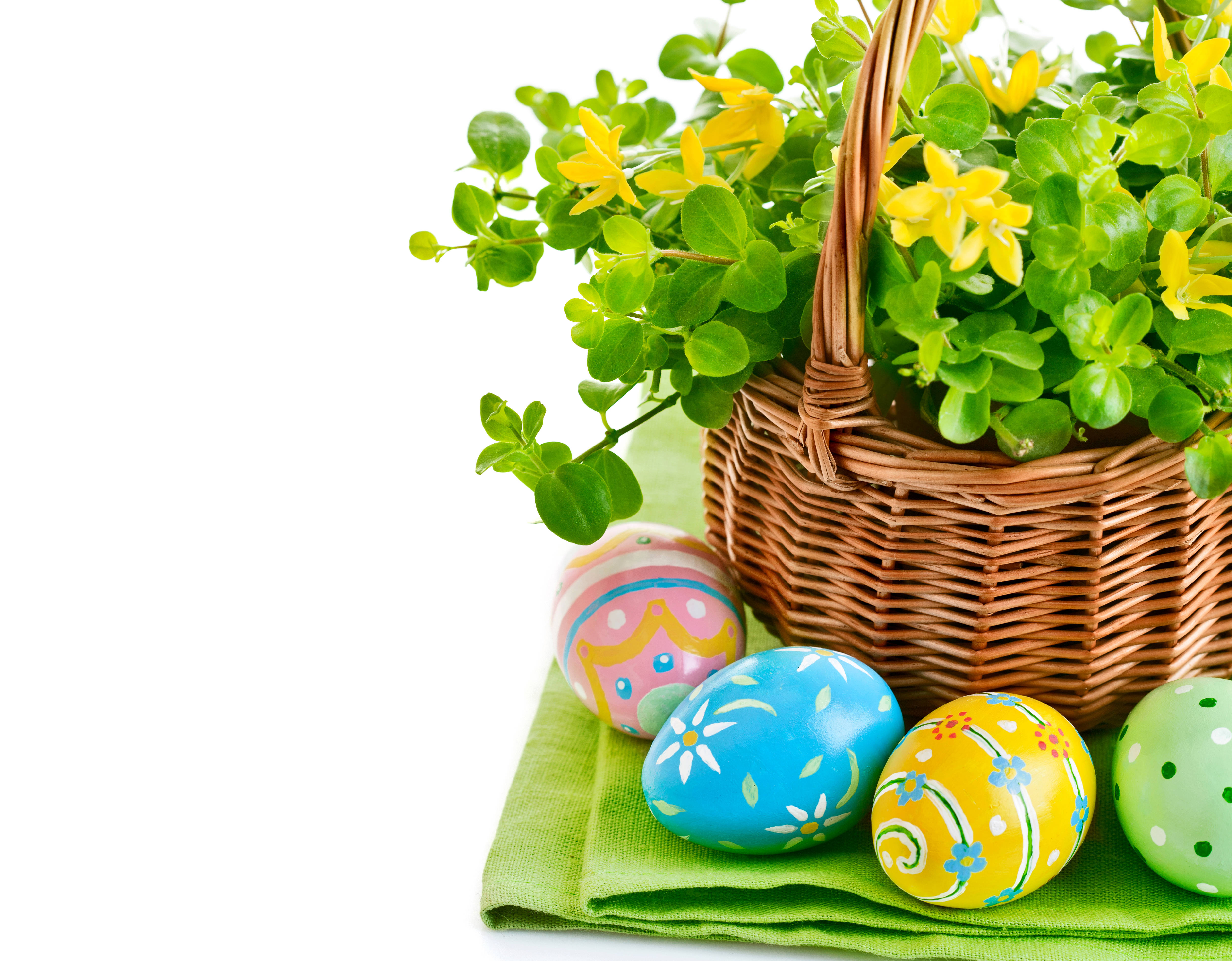 Cute Easter 桌布 壁紙 — 一個柳條籃子裝滿了綠色樹葉和黃色花朵，旁邊有四個色彩鮮豔的復活節彩蛋，放在一塊綠色布上。