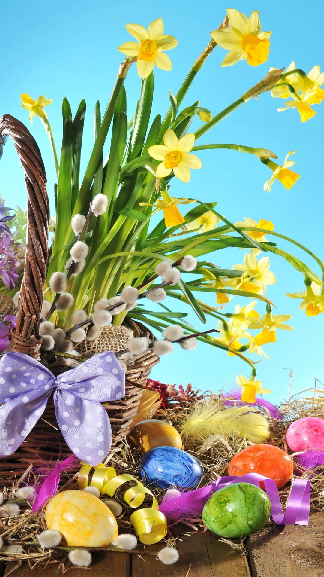Easter Basket 桌布 壁紙 — 一個柳條籃子裝滿了黃色水仙花、貓柳和色彩繽紛的復活節彩蛋，背景是明亮的藍天。
