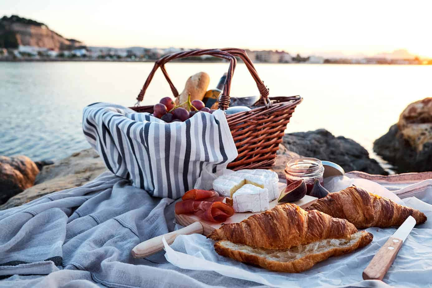 picnic 桌布 壁紙 — 一個柳條野餐籃和美食拼盤在日落時分放在水邊的毯子上。