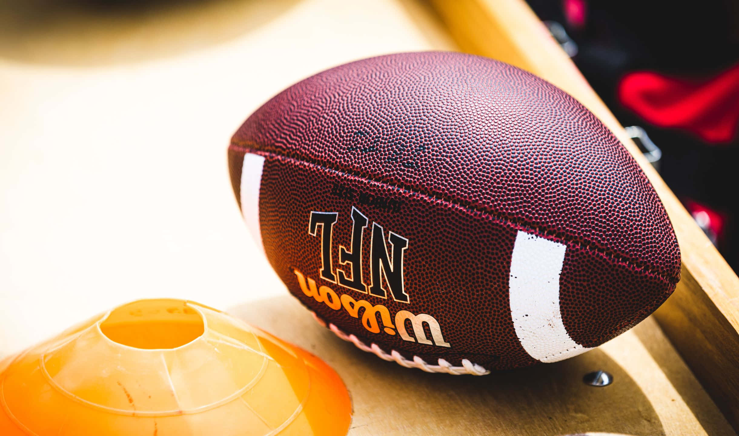 2440x1440 Football 桌布 壁紙 — 一個栗色NFL足球的特寫，旁邊放著一個橙色錐體在木質表面上。
