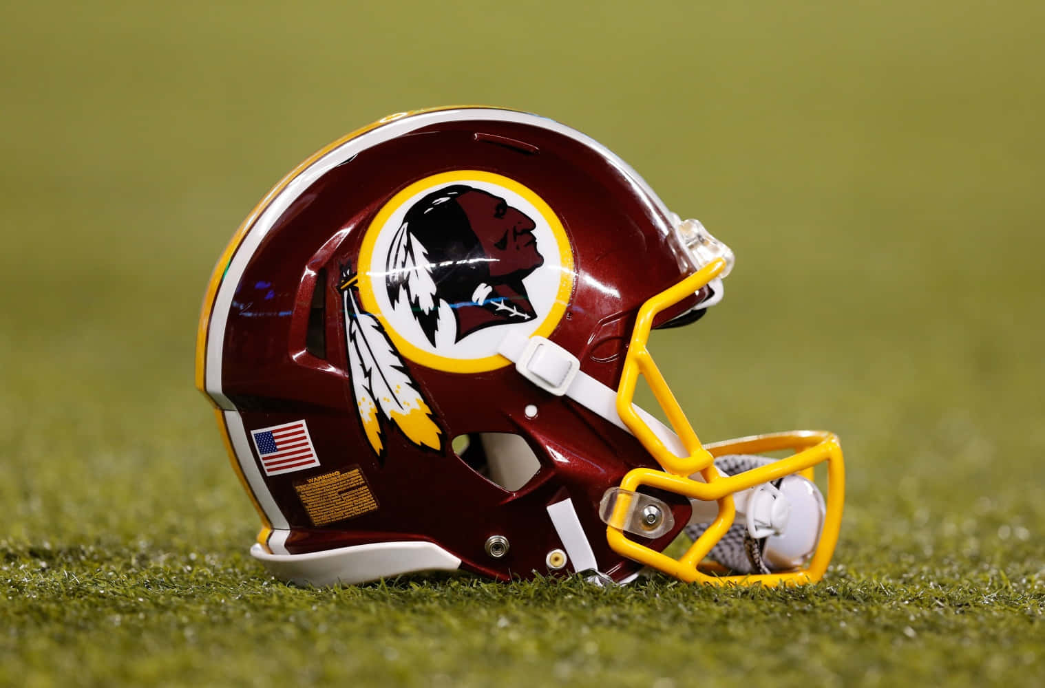 Washington Football 桌布 壁紙 — 一個栗色的華盛頓美式足球隊頭盔，配有黃色面罩，放在鮮綠色的草地上。