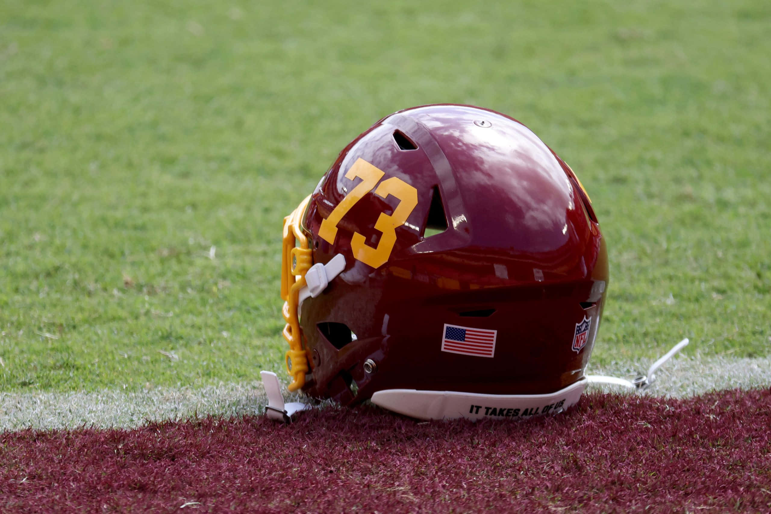 Washington Football 桌布 壁紙 — 一個栗色美式足球頭盔（號碼73）放在球場的端區草地上，倒映著天空的雲朵。