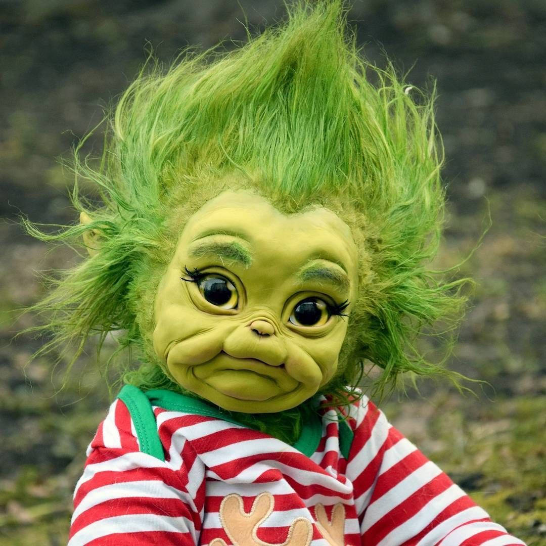 Baby Grinch 桌布 壁紙 — 一個格林奇娃娃的特寫，擁有亮綠色頭髮和紅白條紋襯衫，背景是模糊的戶外景色。
