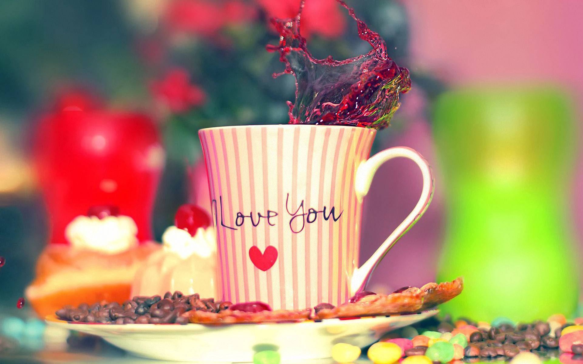 愛心 桌布 壁紙 — 一個條紋杯，上面有「Love You」字樣，從杯緣噴出鮮紅色的液體，周圍有咖啡豆和彩色糖果。