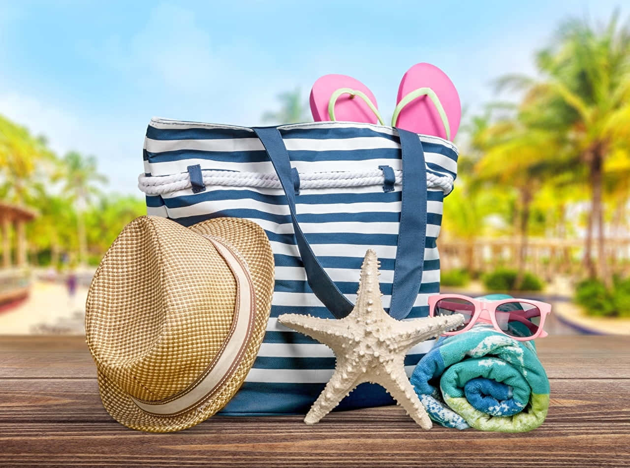Beach Bag 桌布 壁紙 — 一個條紋沙灘袋和粉色人字拖放在木桌上，旁邊有草帽、海星、太陽眼鏡和捲起的毛巾，背景是棕櫚樹。