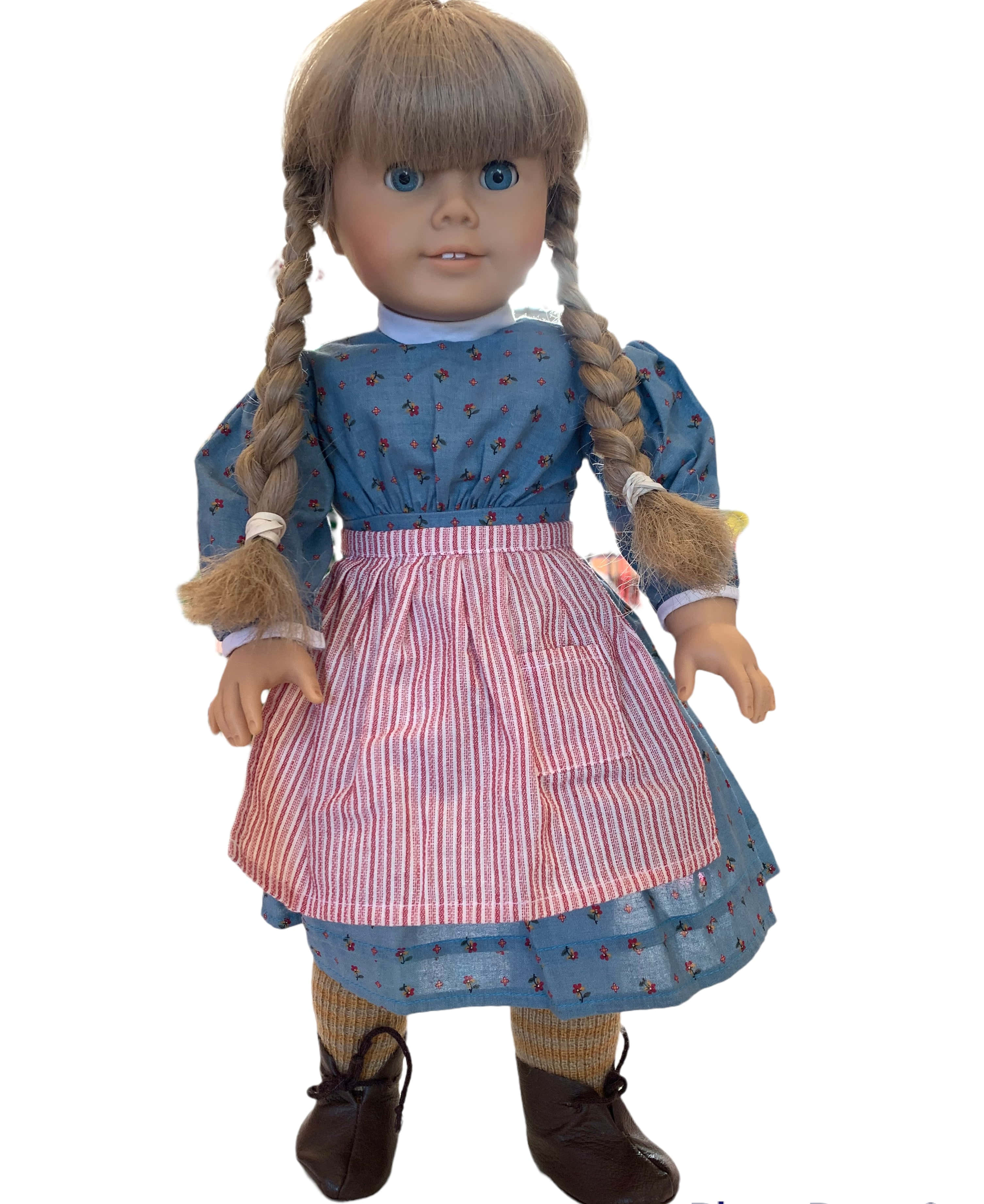american girl 桌布 壁紙 — 一個梳著辮子棕色頭髮的洋娃娃，穿著藍色碎花裙，搭配粉紅色條紋圍裙和棕色鞋子。