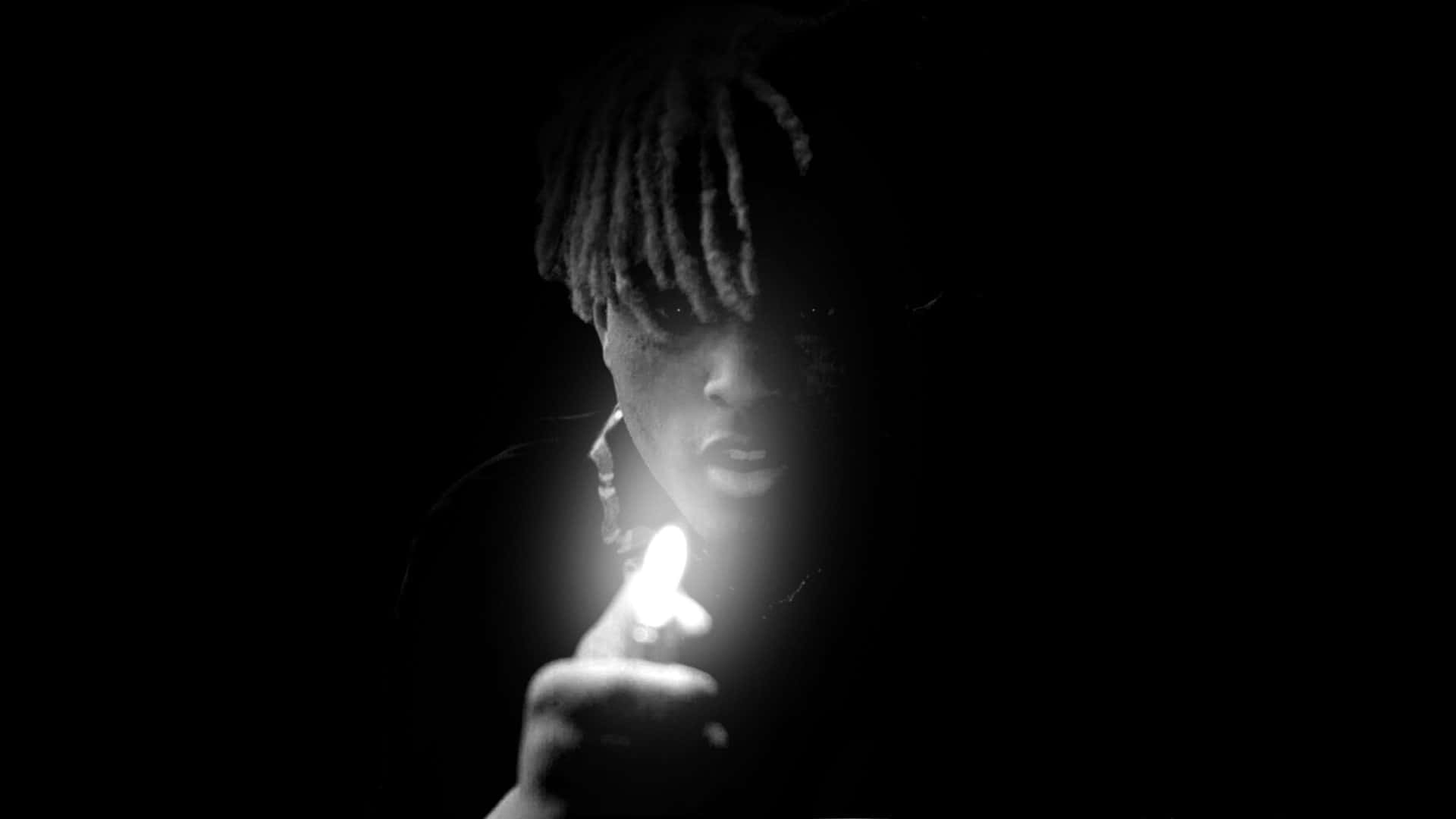 XXXTENTACION 桌布 壁紙 — 一個梳著辮子的人手持點燃的打火機，背景為黑色，戲劇性的光線投射在他們的臉上。