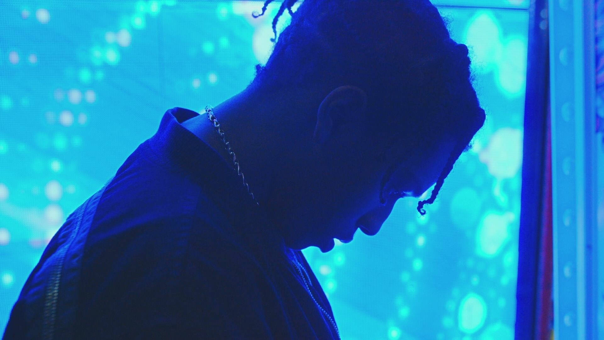 rocky 桌布 壁紙 — 一個梳著辮子頭的人以剪影形式出現在發光的藍色數位背景前，帶有散景燈光。