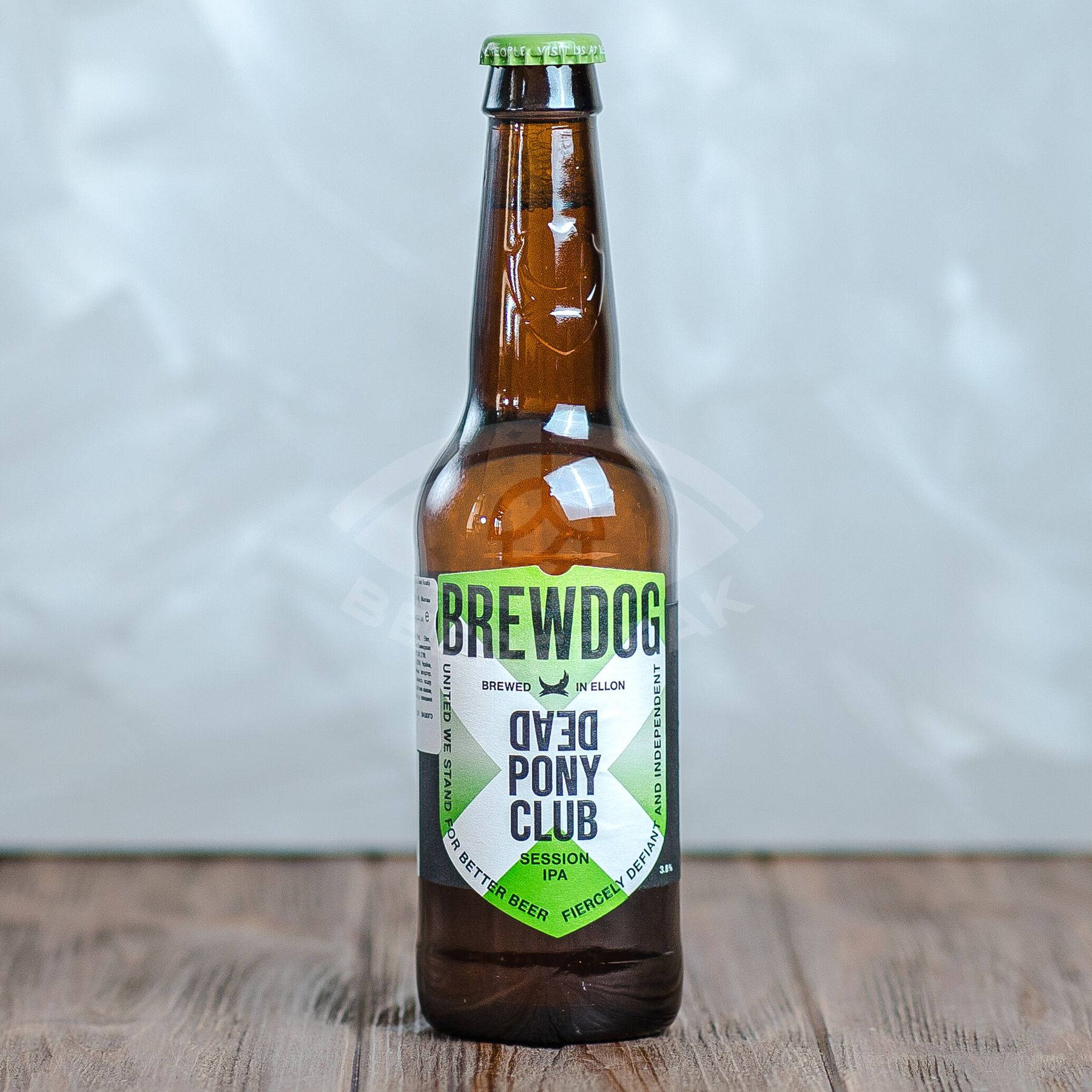 Drink 桌布 壁紙 — 一個棕色玻璃 BrewDog Dead Pony Club Session IPA 啤酒瓶，帶綠色瓶蓋，放在木質表面上，背景為柔和的灰色。