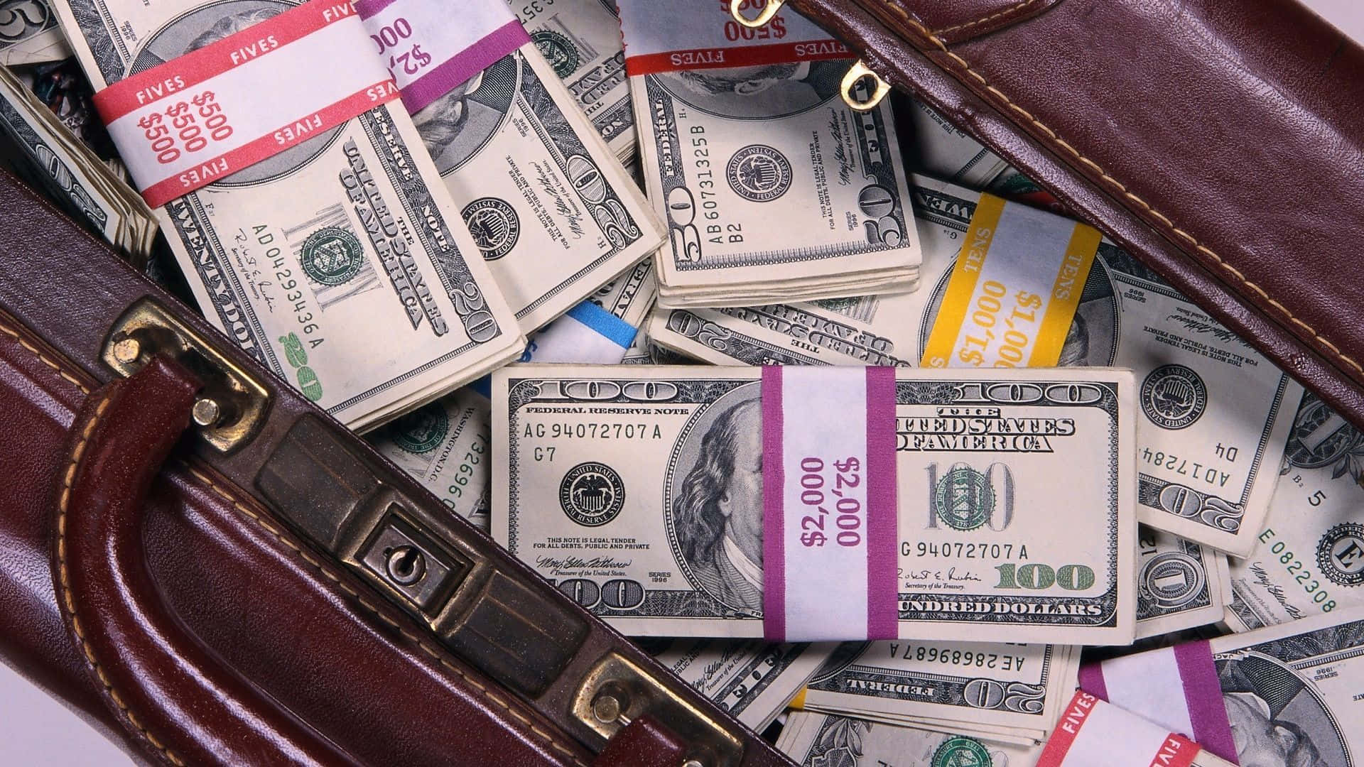 Money Bag 桌布 壁紙 — 一個棕色皮革公文包灑出一疊疊的美鈔，包括五元和一百元紙幣，散落在白色表面上。