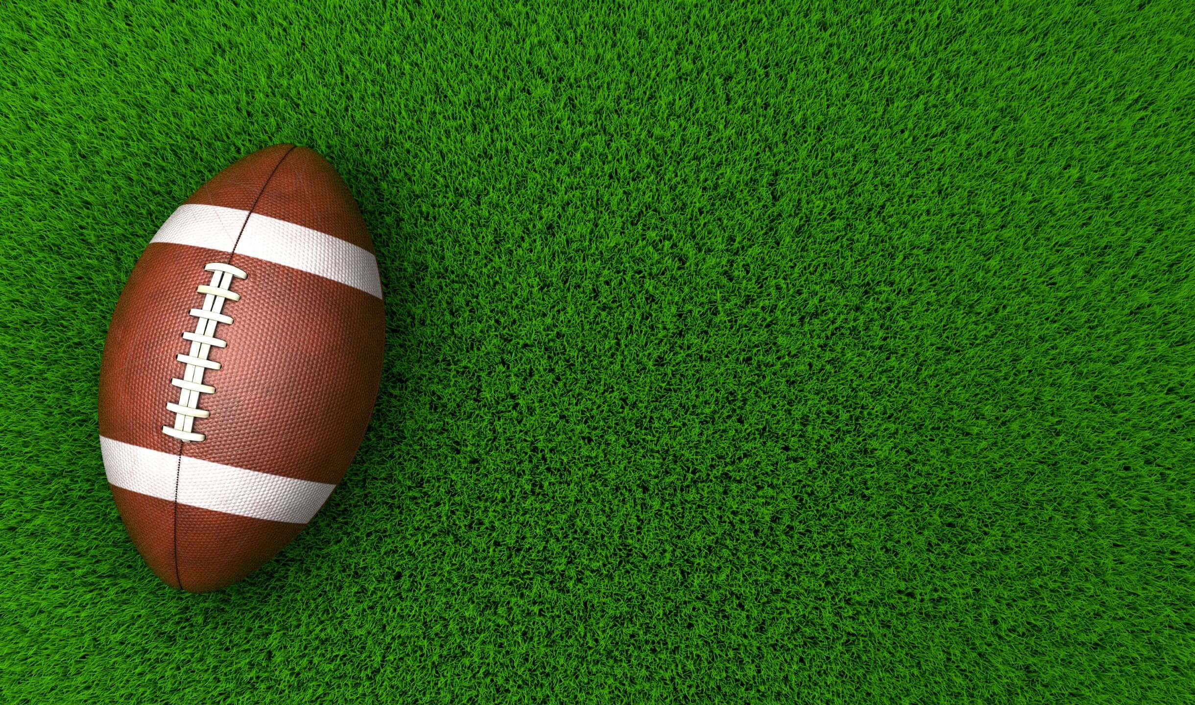 2440x1440 Football 桌布 壁紙 — 一個棕色皮革美式足球，帶有白色鞋帶和條紋，放在充滿活力的綠色草地上。