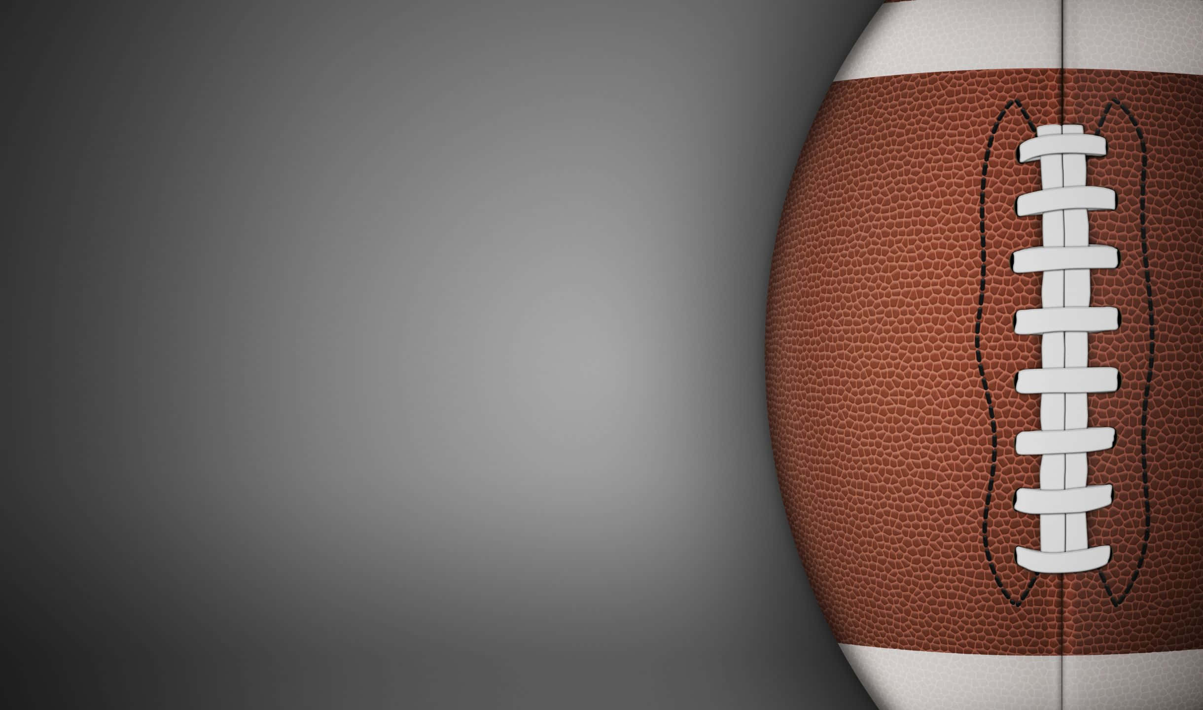 2440x1440 Football 桌布 壁紙 — 一個棕色皮革美式足球的特寫，帶有白色鞋帶，背景為漸變灰色。