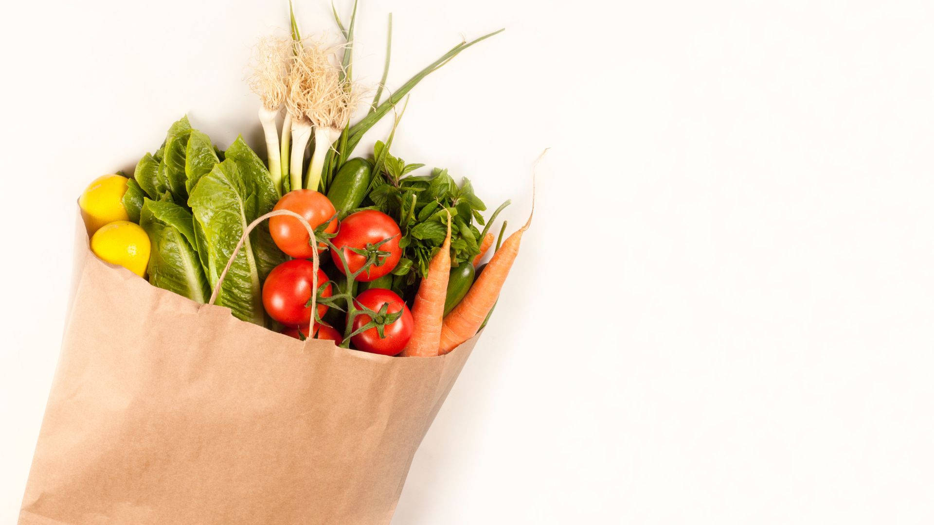 Vegetables 桌布 壁紙 — 一個棕色紙袋，裝滿新鮮色彩繽紛的蔬菜，如番茄、紅蘿蔔和生菜，放在潔淨的白色背景前。