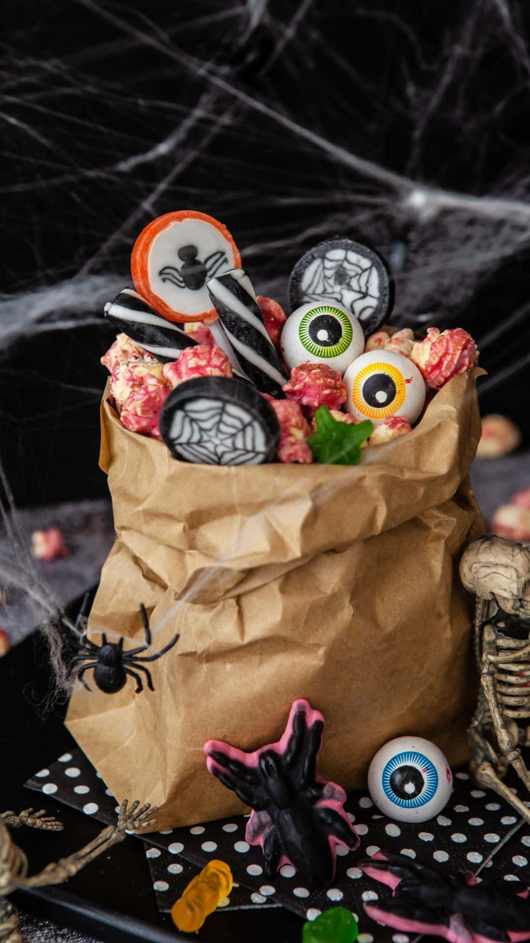 Trick Or Treat Bags 桌布 壁紙 — 一個棕色紙袋，裝滿萬聖節糖果和恐怖裝飾，背景是黑色蜘蛛網。