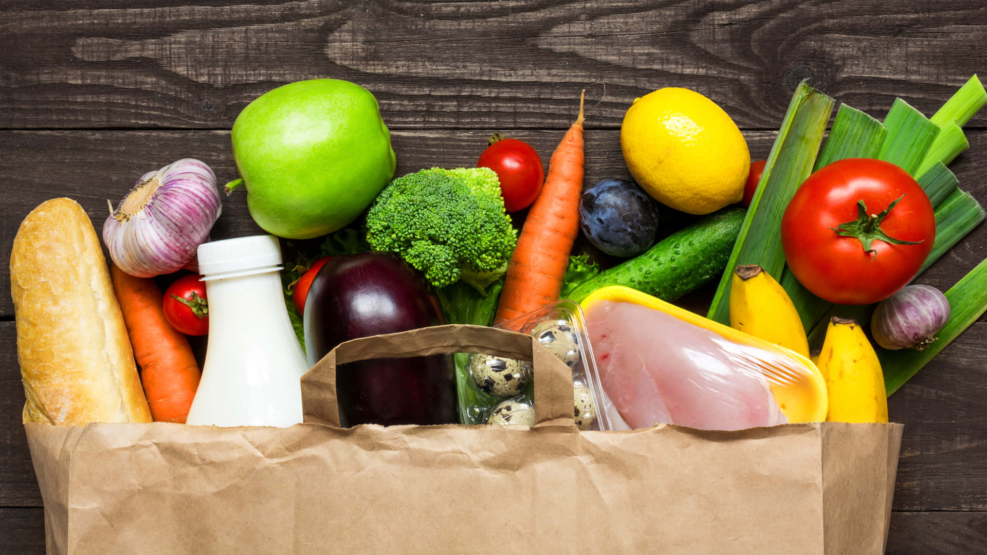 Healthy Food 桌布 壁紙 — 一個棕色紙購物袋，裝滿色彩繽紛的新鮮農產品、乳製品和肉類，放在深色木質表面上。