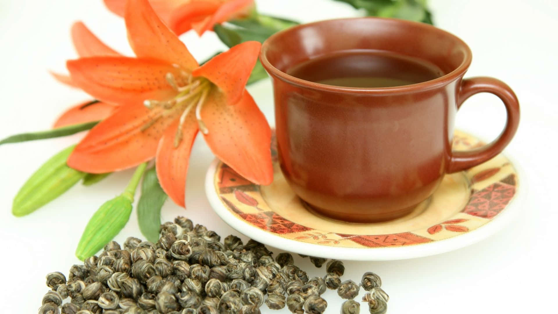 Floral Tea 桌布 壁紙 — 一個棕色陶瓷茶杯放在有圖案的碟子上，旁邊有鮮豔的橙色百合和散裝茶葉。