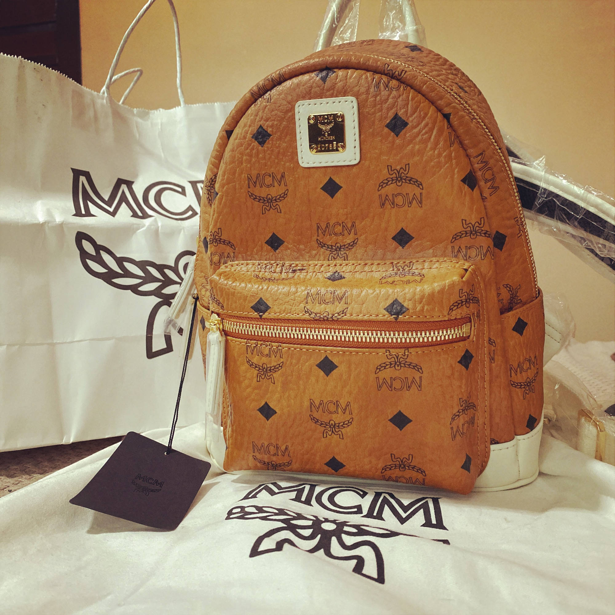 Leather Texture 桌布 壁紙 — 一個棕褐色MCM後背包帶有重複標誌圖案，放在品牌購物袋和紙巾上。