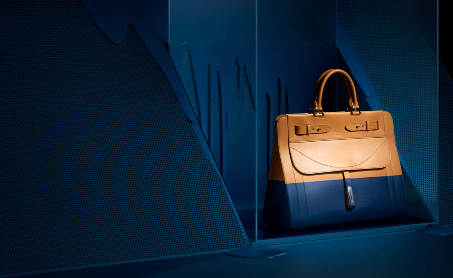 Luxury Brands 桌布 壁紙 — 一個棕褐色和深藍色皮革手提包在時尚的玻璃陳列櫃中展示，並配有戲劇性的藍色燈光。