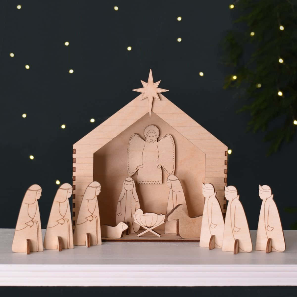 Nativity Scene 桌布 壁紙 — 一個極簡主義的木製耶穌誕生場景，帶有鏤空人物和馬廄頂上的星星，背景為黑暗，配有閃爍燈光和松樹枝。