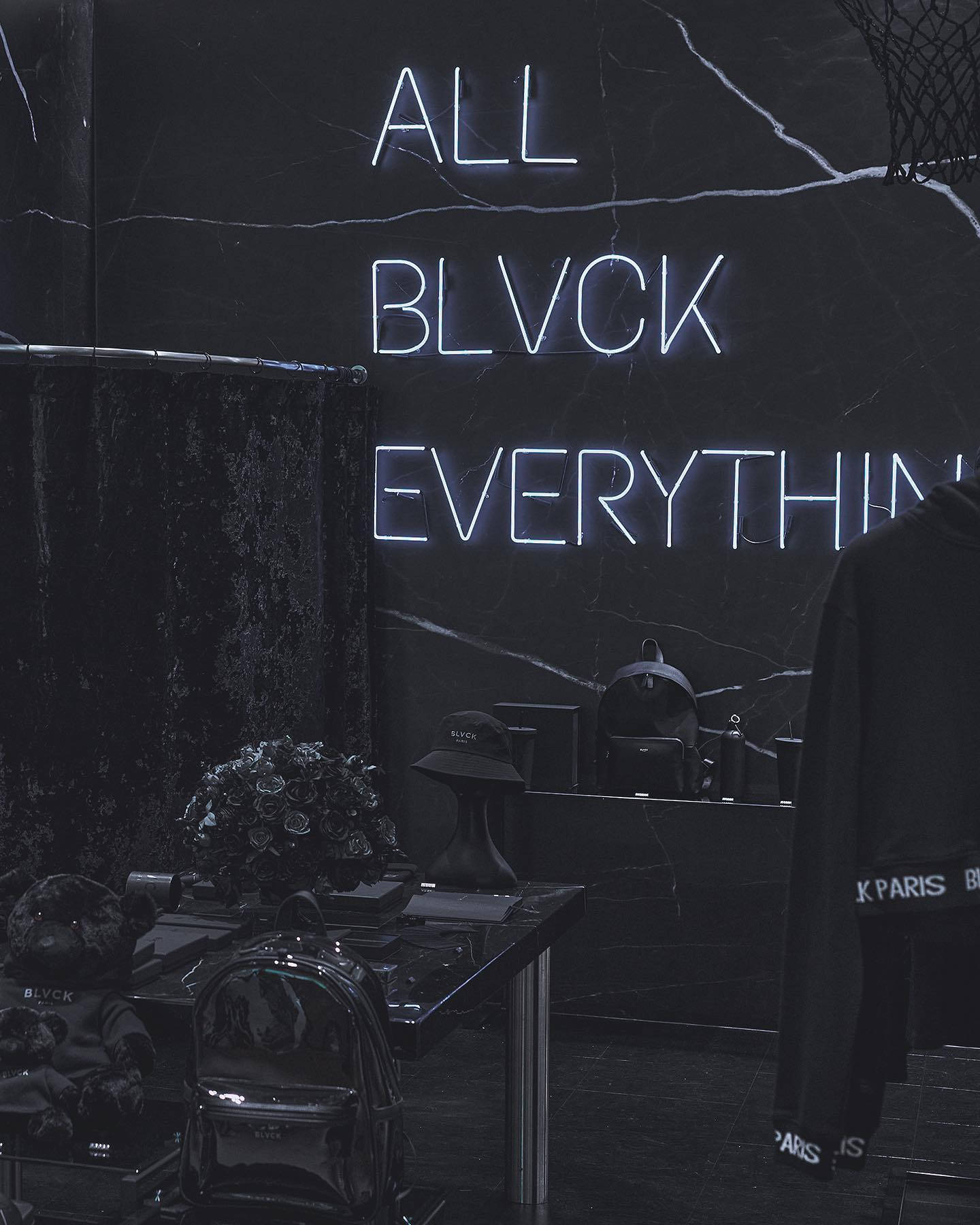 Blvck Paris 桌布 壁紙 — 一個極簡主義的黑色大理石房間，由發光的霓虹文字 'ALL BLVCK EVERYTHING' 照亮，並展示時尚物品。