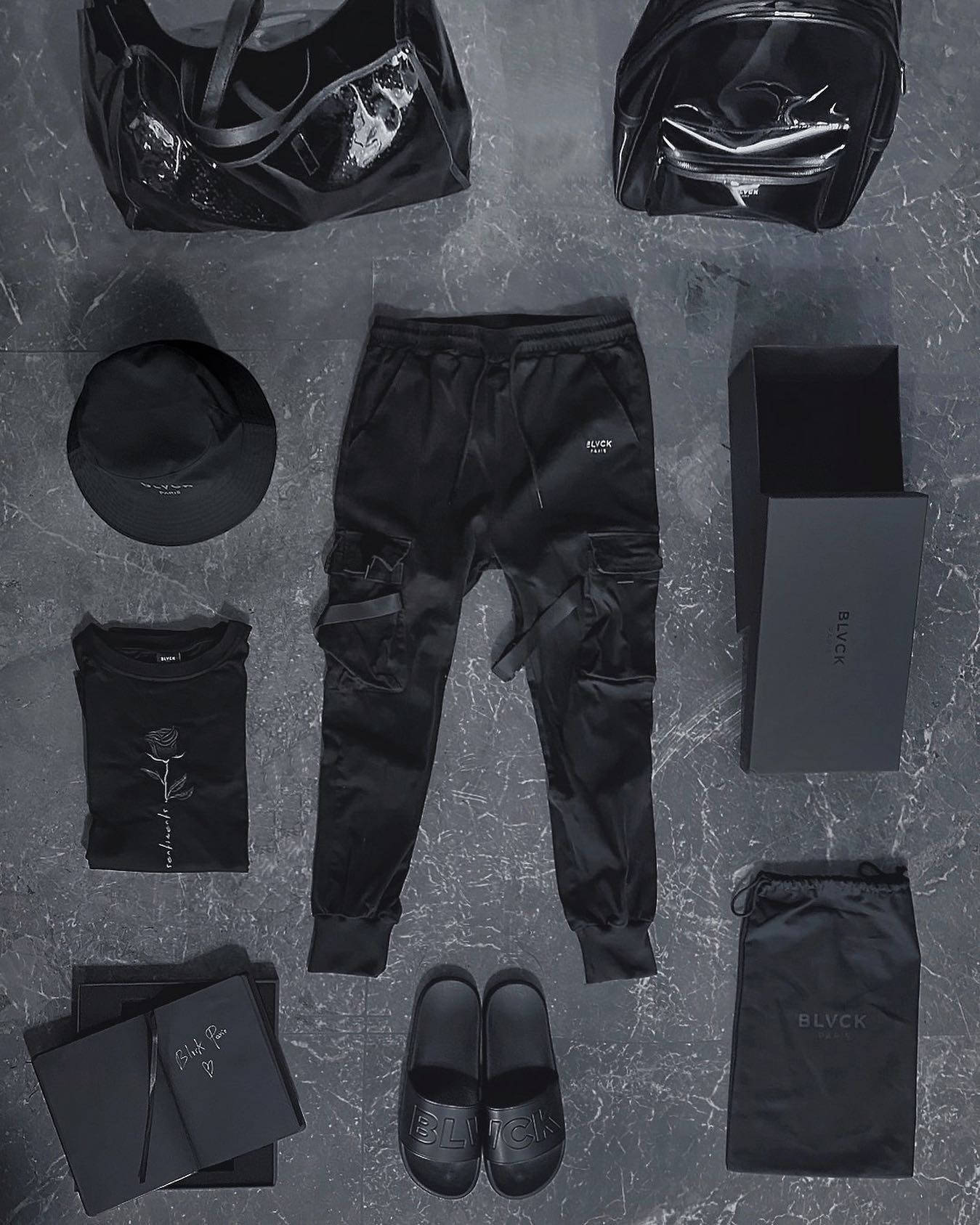 outfit 桌布 壁紙 — 一個極簡主義的黑色時尚平鋪圖，展示BLVCK品牌的服裝配飾和手提包，排列在灰色大理石表面上。