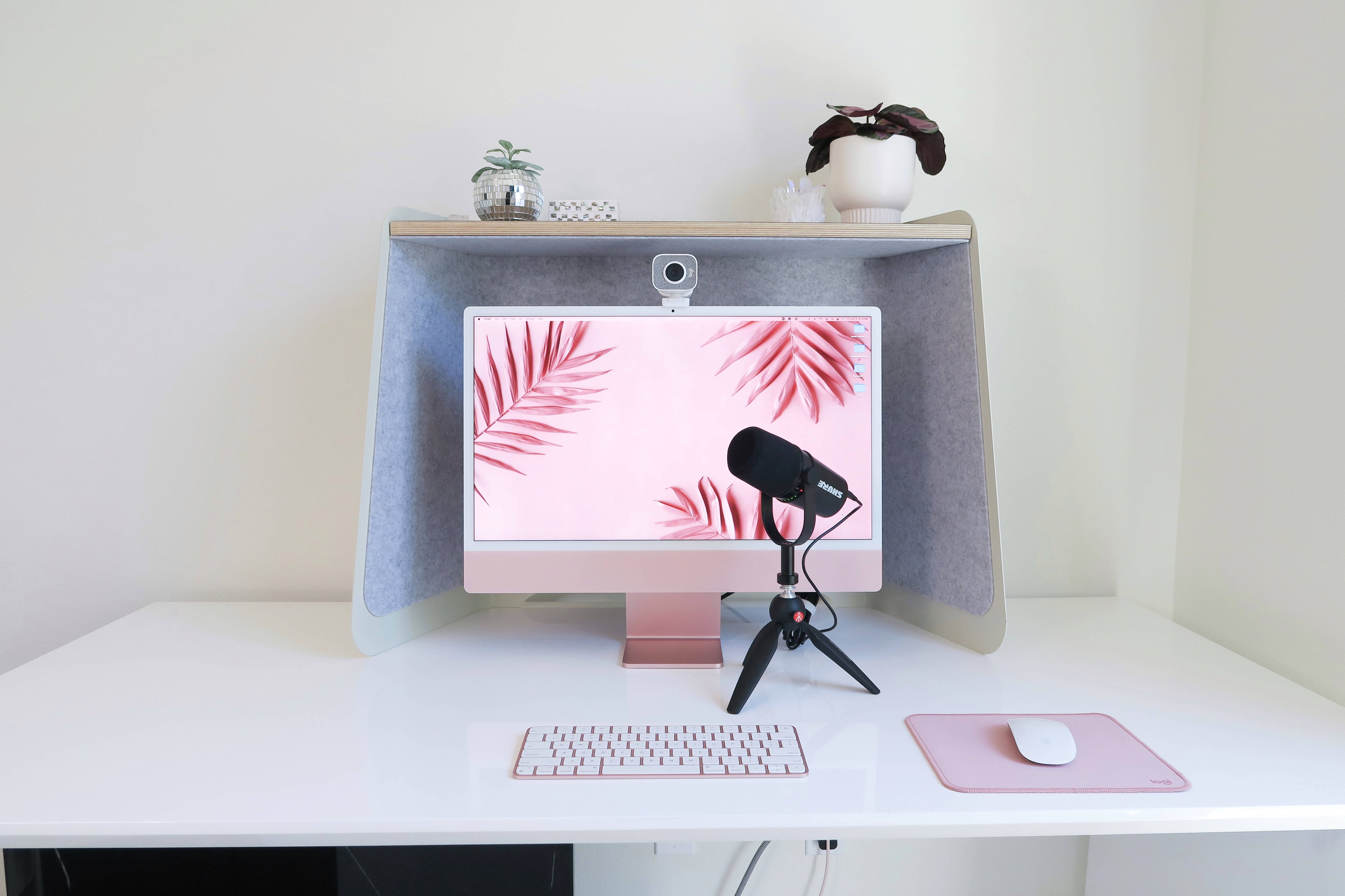 Webcam 桌布 壁紙 — 一個極簡家居辦公室設置，配備玫瑰金 iMac 顯示粉紅色棕櫚葉、三腳架上的黑色麥克風和白色桌面配件。