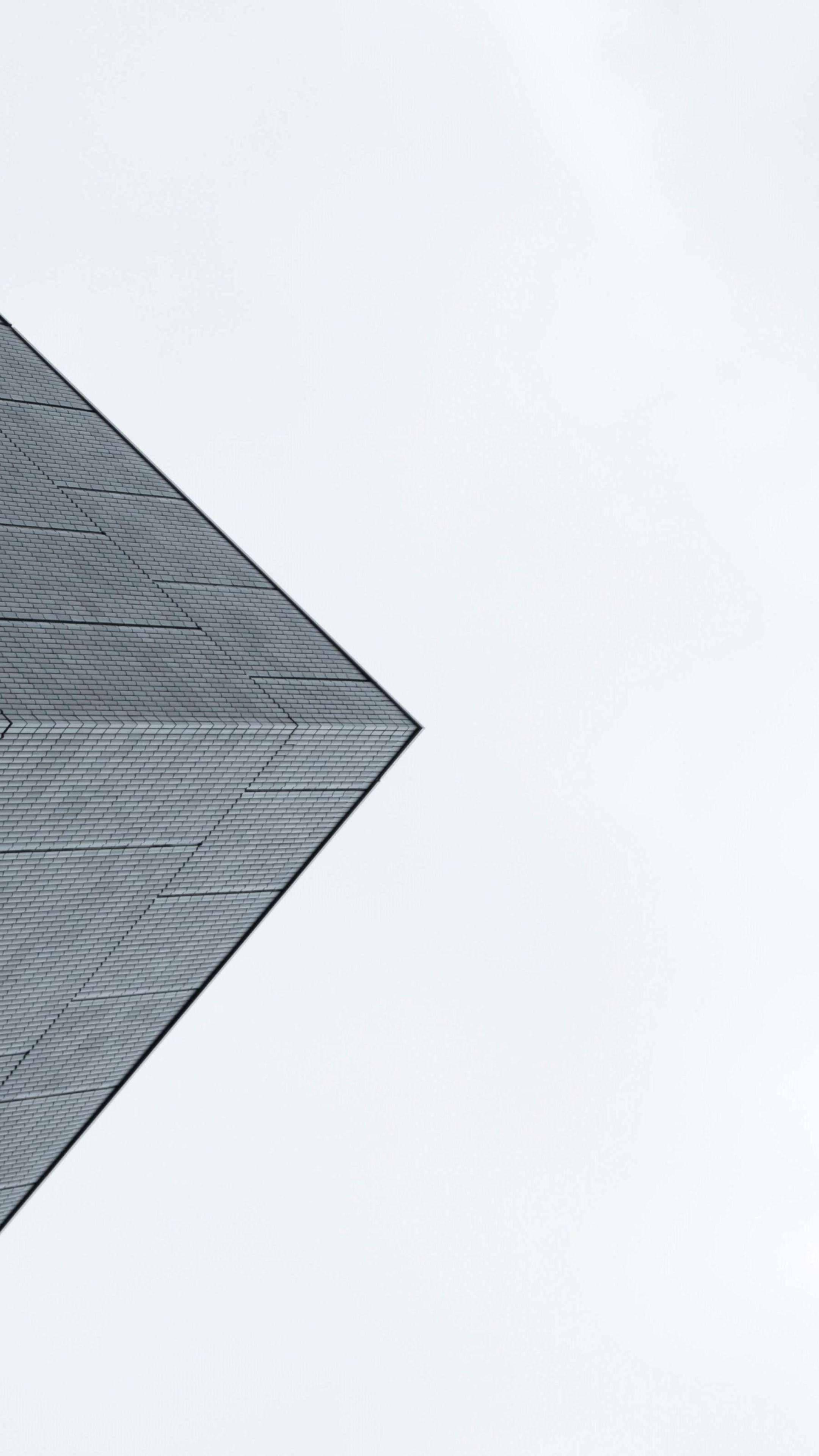 Minimalist Phone 桌布 壁紙 — 一個極簡幾何屋頂角落，帶有紋理的灰色瓦片，在廣闊蒼白的天空下形成銳利角度。