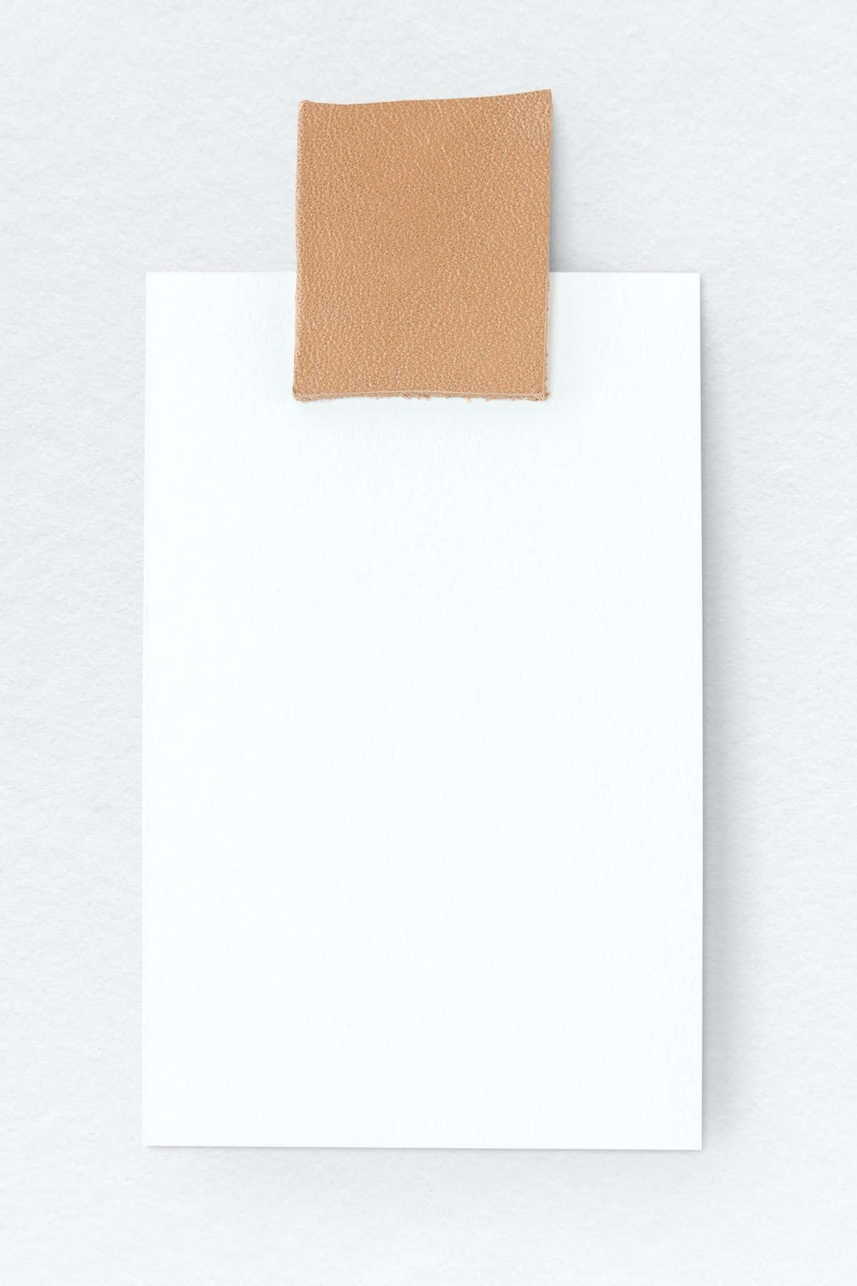 paper 桌布 壁紙 — 一個極簡的構圖，米色皮革補丁夾在白色卡片上，背景為有紋理的白色。