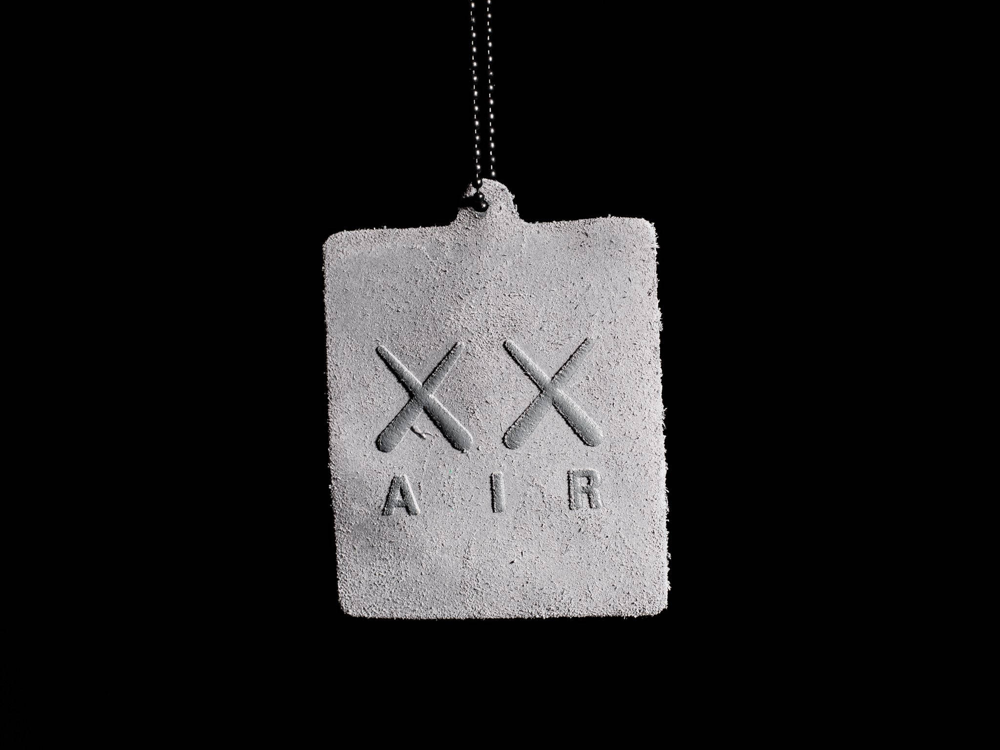 KAWS 桌布 壁紙 — 一個極簡的水泥標籤，帶有浮雕X和AIR，掛在純黑背景上。