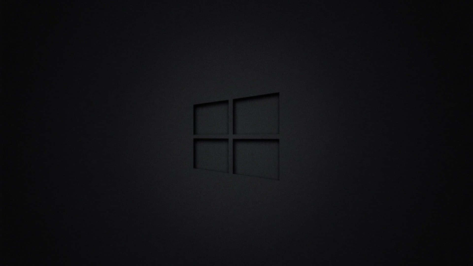 桌布 壁紙 — 一個極簡的深灰色Windows標誌，在柔和環境光下微妙地壓印在帶紋理的黑色牆壁上。