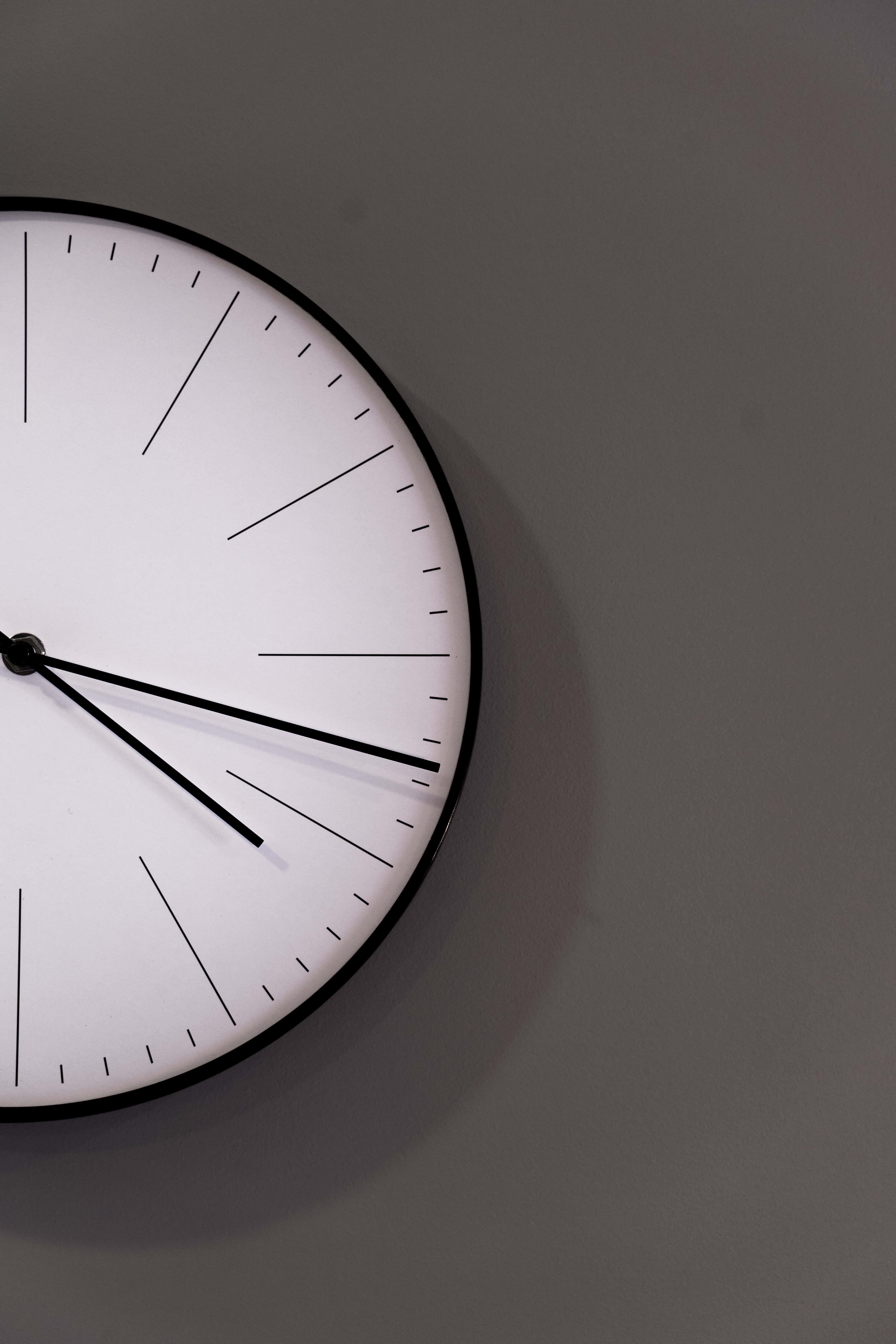 Clocks 桌布 壁紙 — 一個極簡的黑白掛牆鐘，配有細長指針和幾何標記，掛在柔和的灰色牆上。