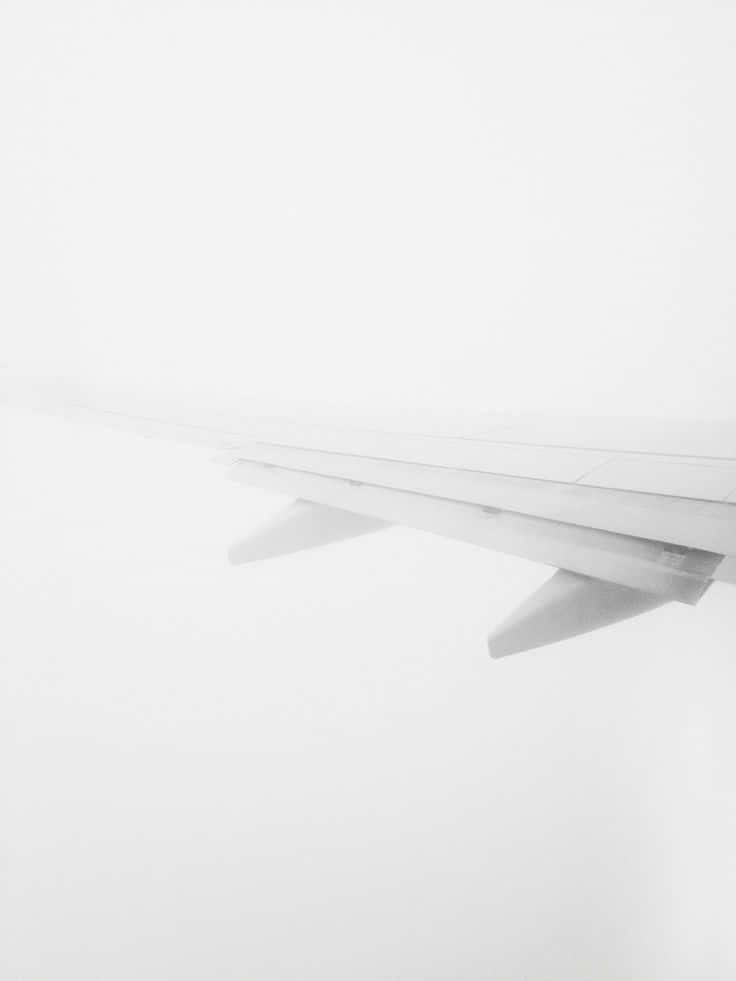 白色美學動圖 桌布 壁紙 — 一個極簡的黑白視角，飛機機翼劃破廣闊的白色雲層天花板。