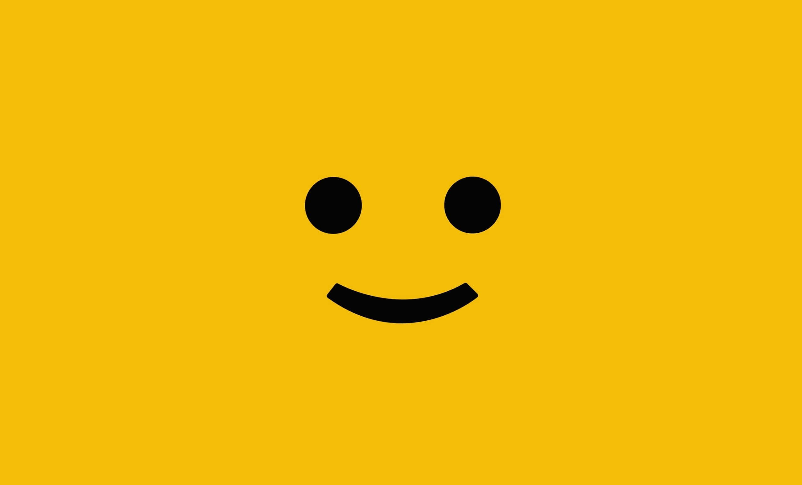 Lego Face 桌布 壁紙 — 一個極簡的黑色笑臉，有兩點作為眼睛和彎曲的嘴巴，居中在純黃色背景上。
