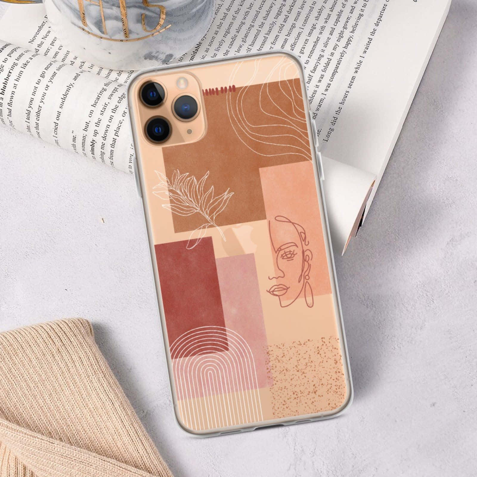 Phone Case 桌布 壁紙 — 一個極簡風格手機殼，帶有抽象陶土幾何形狀和臉部與葉子的線條藝術，放置在打開的書本和針織布料上。