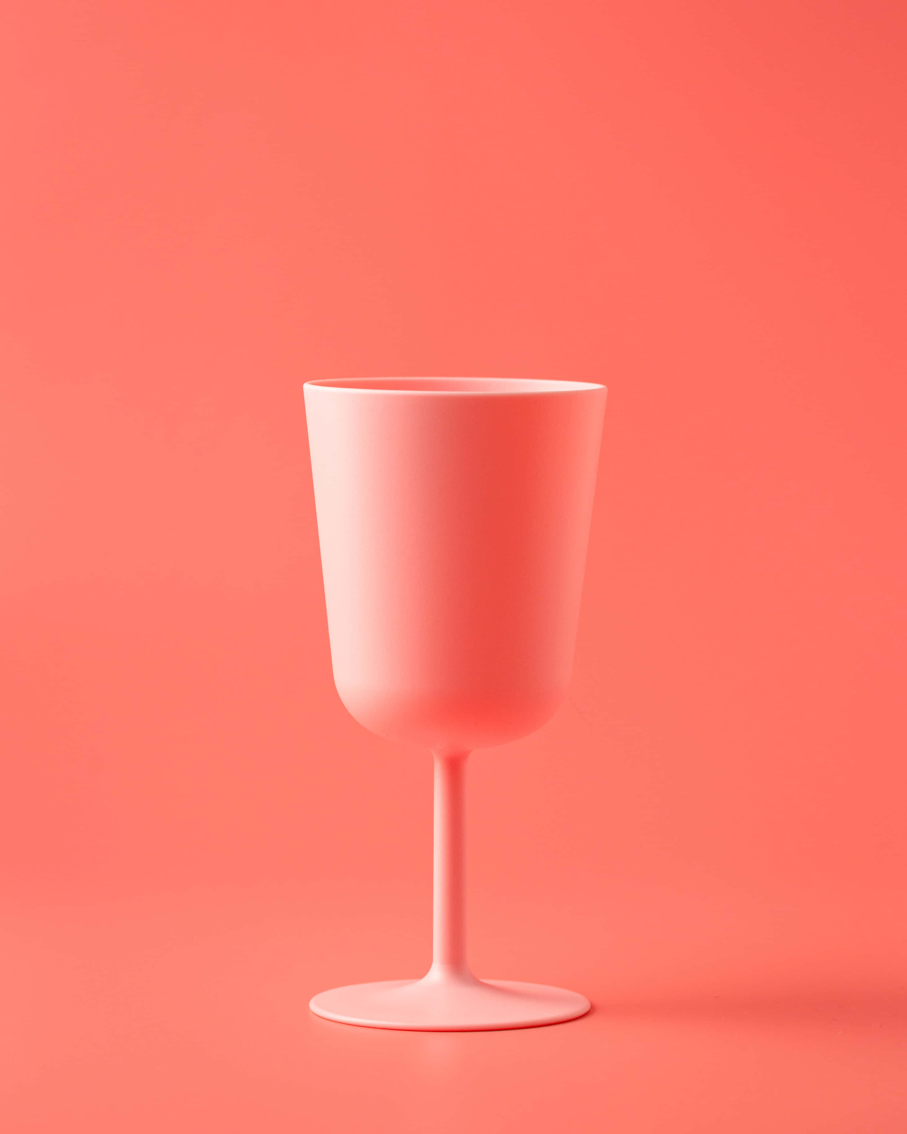 cup 桌布 壁紙 — 一個極簡風格的啞光粉紅酒杯，在柔和光線下居中放置於純珊瑚色背景上。